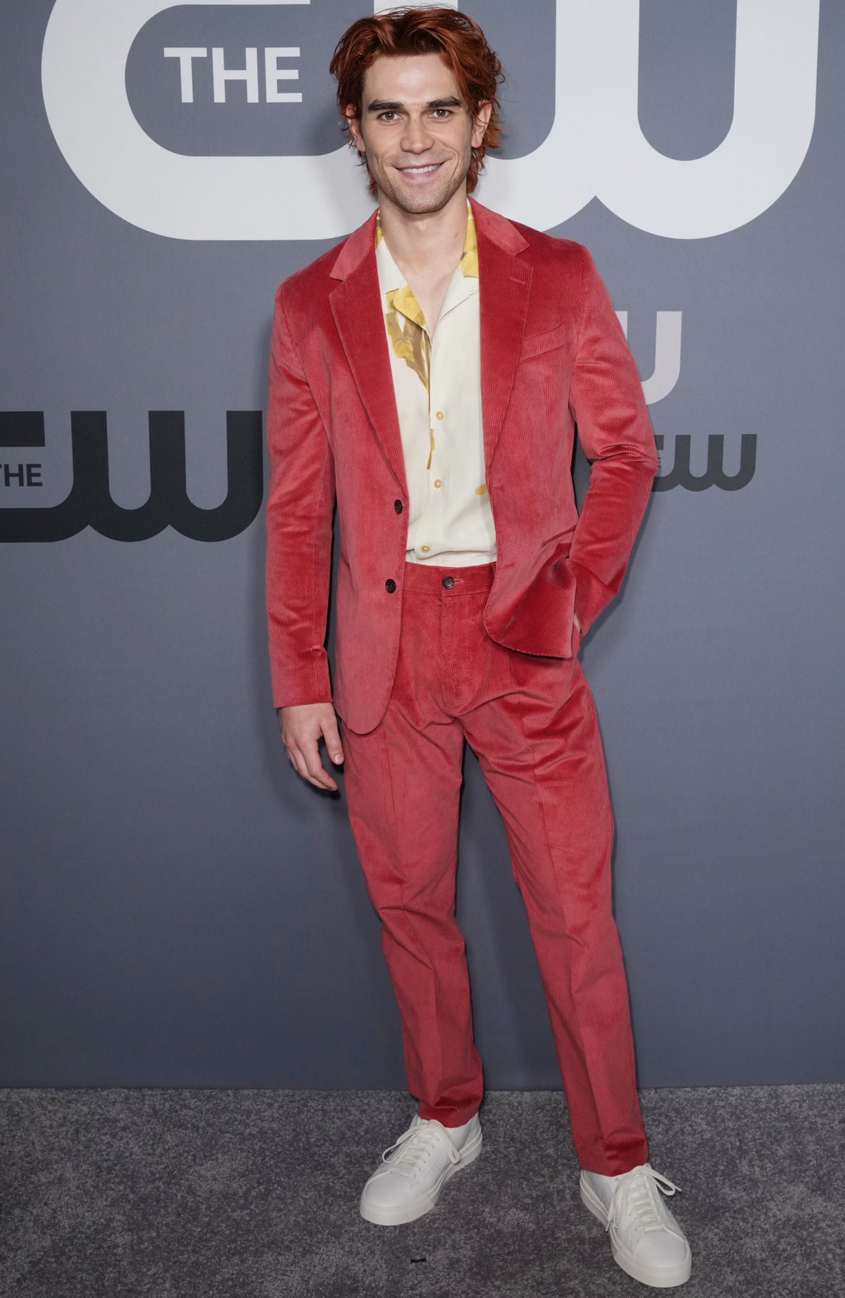 KJ Apa makes a bold statement in a red corduroy suit paired with a printed shirt and white sneakers, blending casual and retro vibes at The CW event