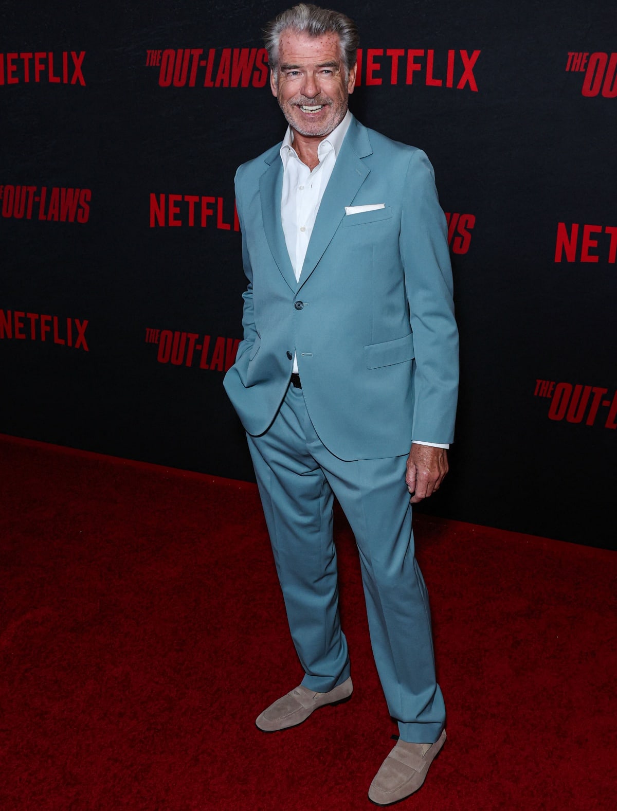 Pierce Brosnan exudes effortless charm in a sleek, light blue suit paired with beige loafers at the premiere of The Out-Laws