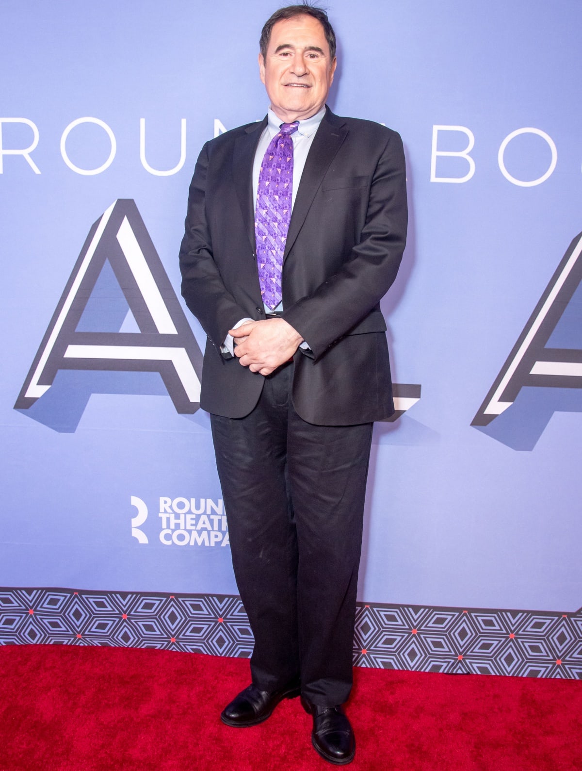 Richard Kind looks sharp in a classic black suit paired with a vibrant purple tie at the 2023 Roundabout Theatre Company Gala