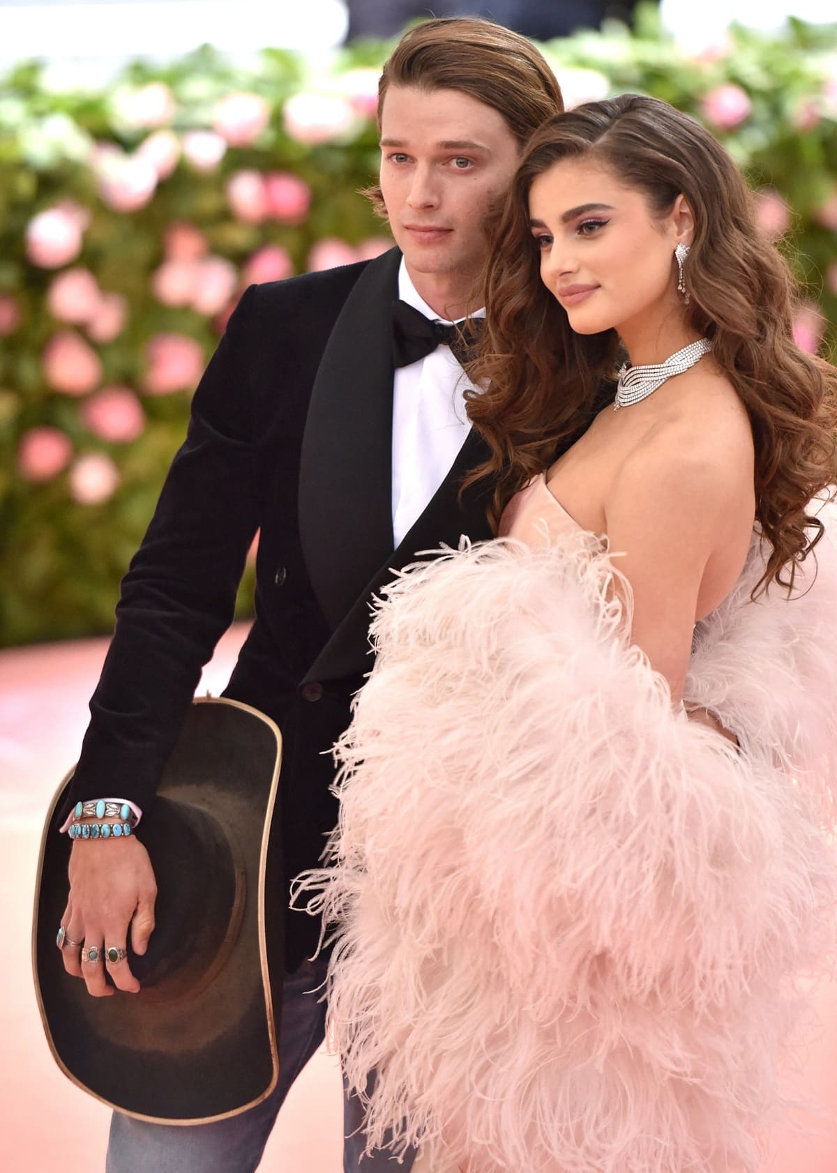 At the 2019 Met Gala "Celebrating Camp: Notes On Fashion" held at The Metropolitan Museum of Art in New York City on May 6, 2019, Patrick Schwarzenegger embraced a country-themed ensemble, whereas Taylor Hill elegantly evoked old-Hollywood allure in a satin slip dress, complemented by a blush feather boa and mesmerizing diamond adornments