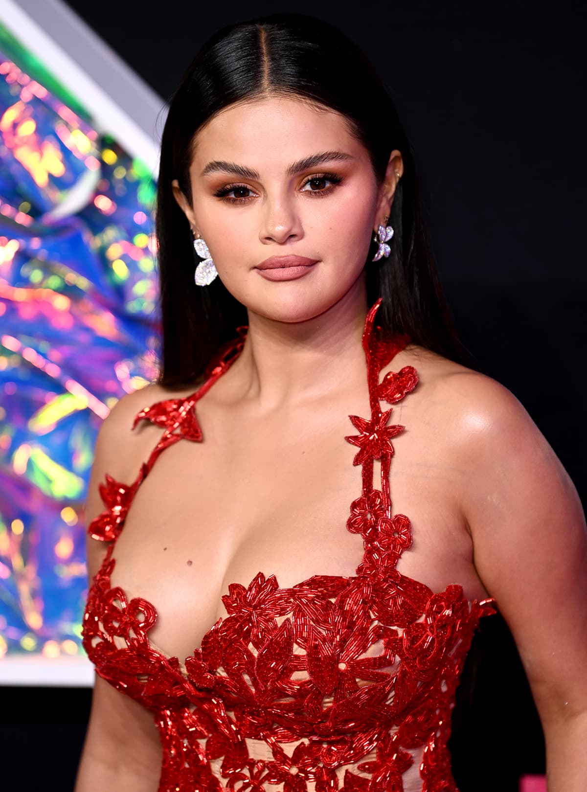 Selena Gomez wears neutral makeup with bronze eyeshadow and nude lipstick and styles her tresses straight and tucked behind her ears