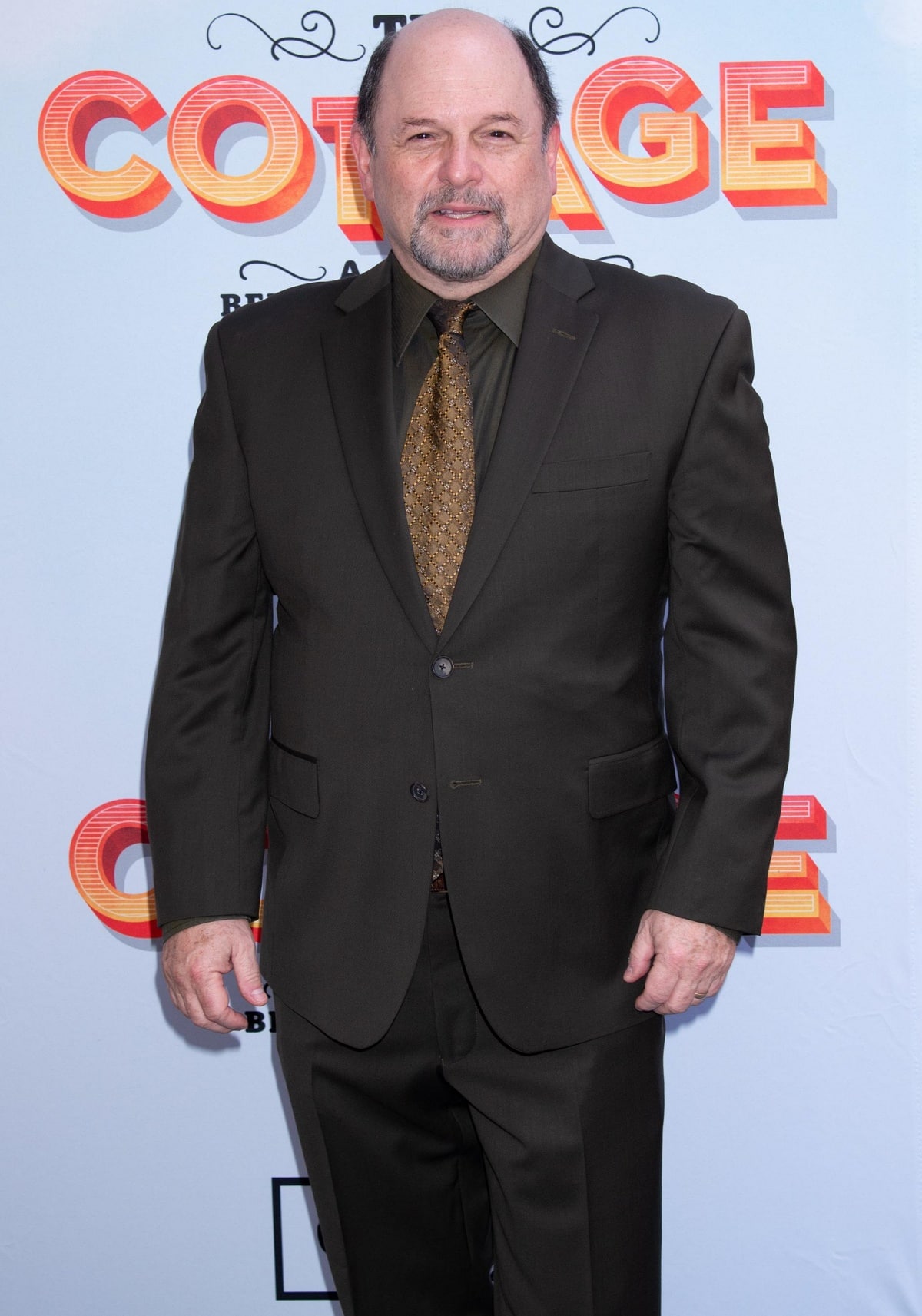 Jason Alexander looks dapper in a dark brown suit paired with a patterned tie, effortlessly pulling off a classic and polished look