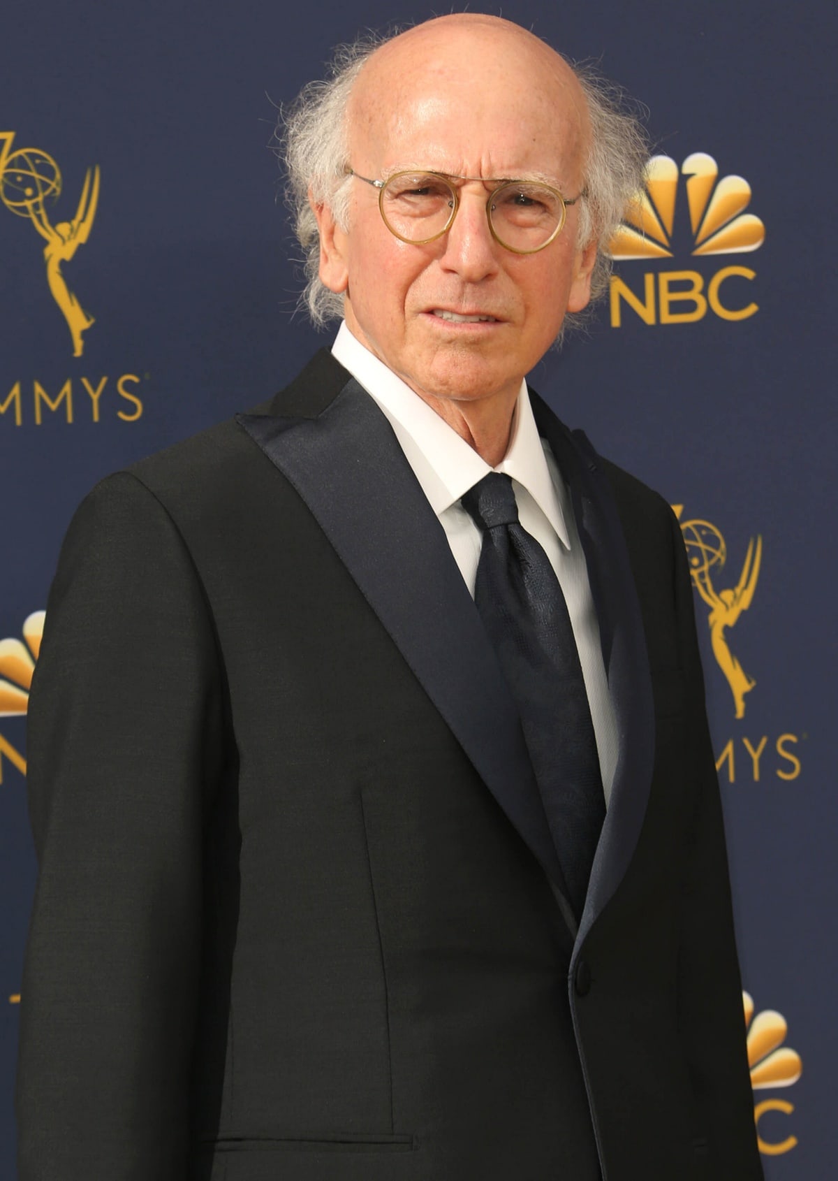 Larry David looks sharp in a classic black tuxedo with satin lapels, paired with a matching tie and his signature round glasses at the Emmy Awards