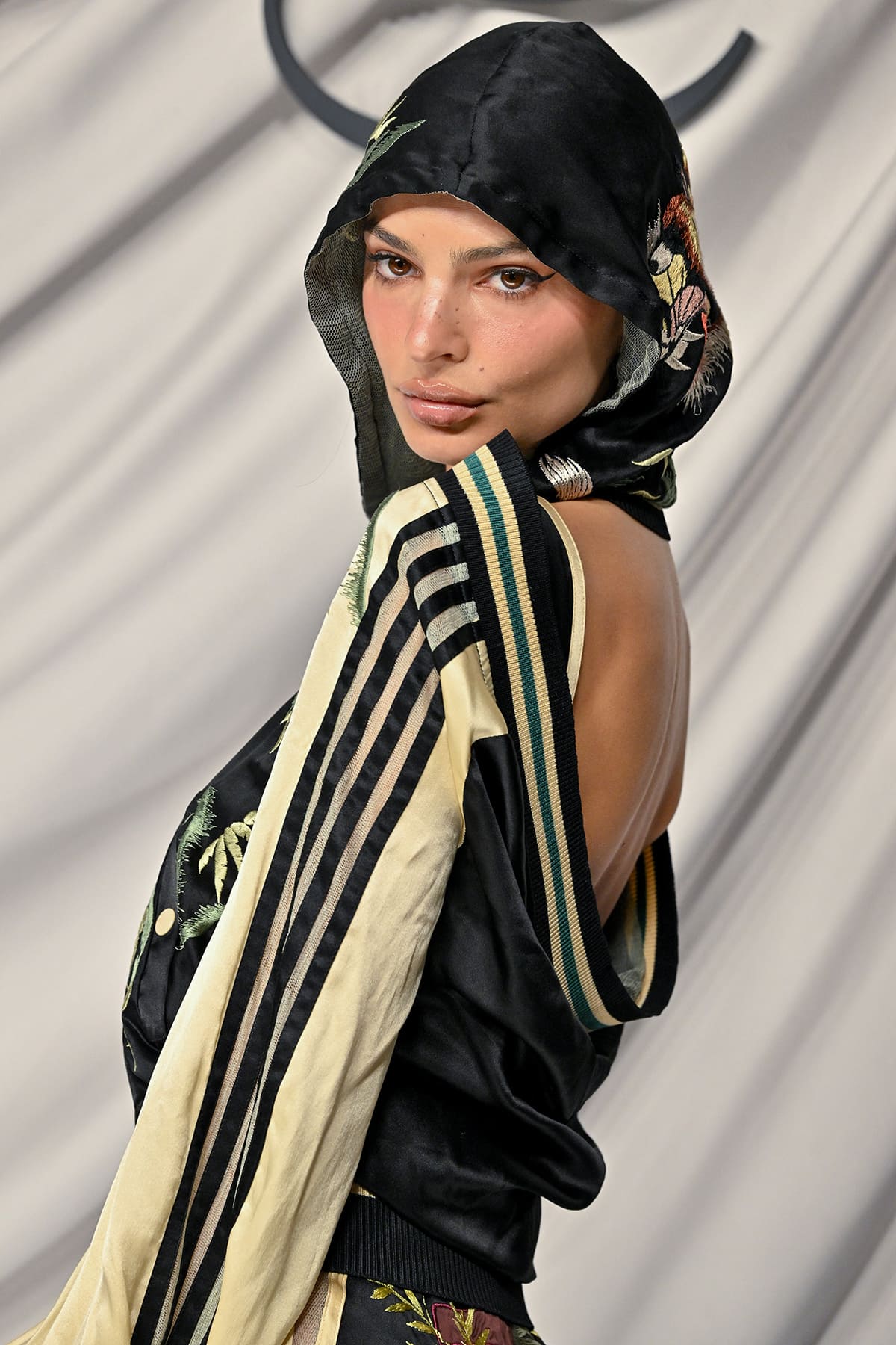Emily Ratajkowski hides her hair underneath her hooded jacket and wears winged eyeliner, nude lip gloss, and faux freckles