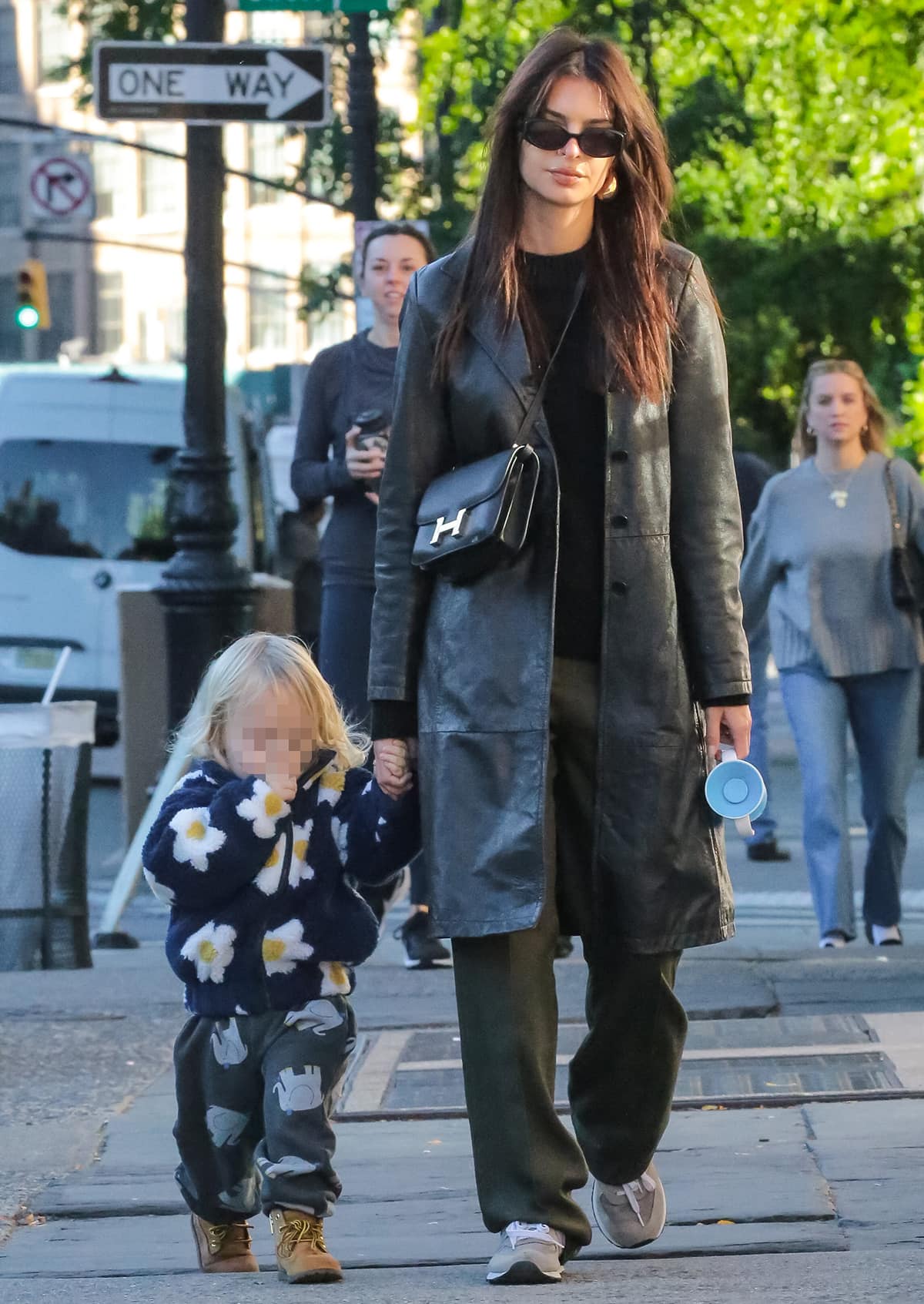 Emily Ratajkowski out and about with her son Sylvester Apollo Bear in an easy autumnal outfit featuring a black leather trench coat, a crewneck sweater, and baggy green pants on October 13, 2023
