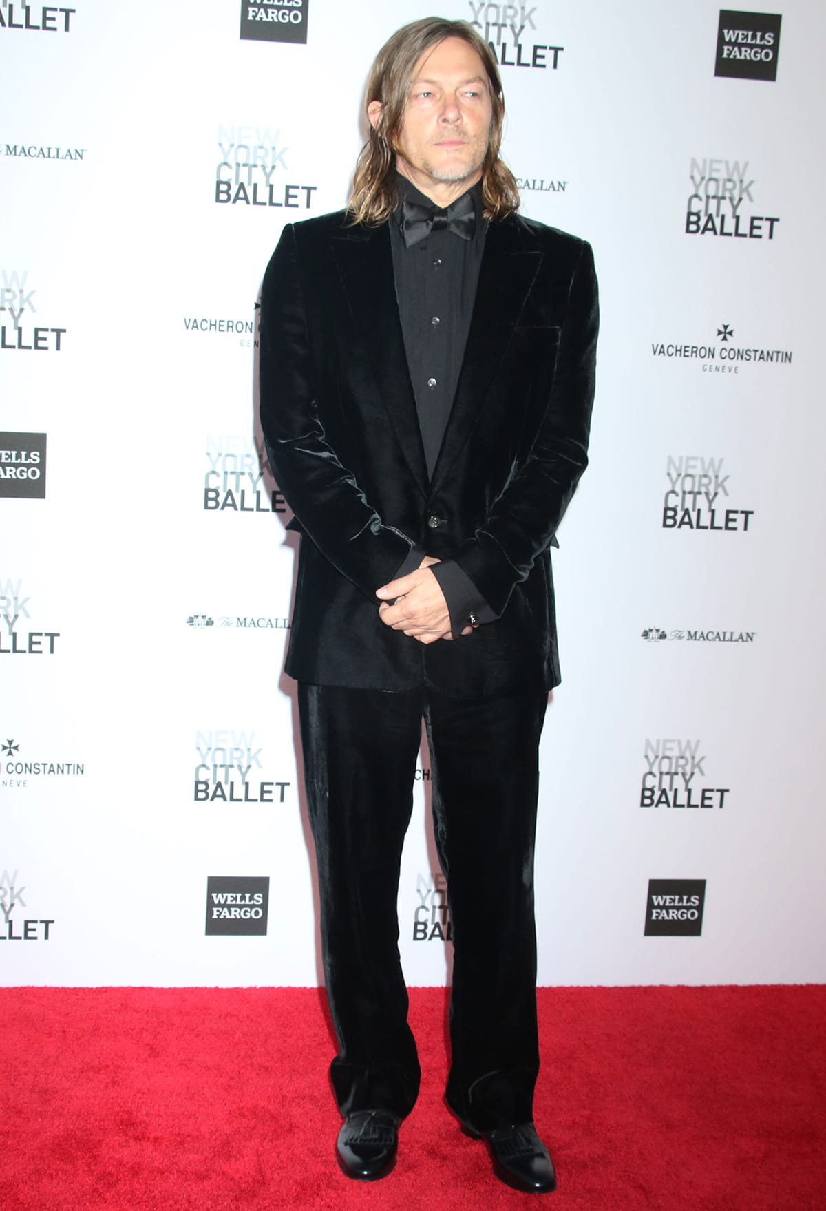 Norman Reedus looks dapper in a black velvet tuxedo suit with a matching bowtie, shirt, and shiny dress shoes