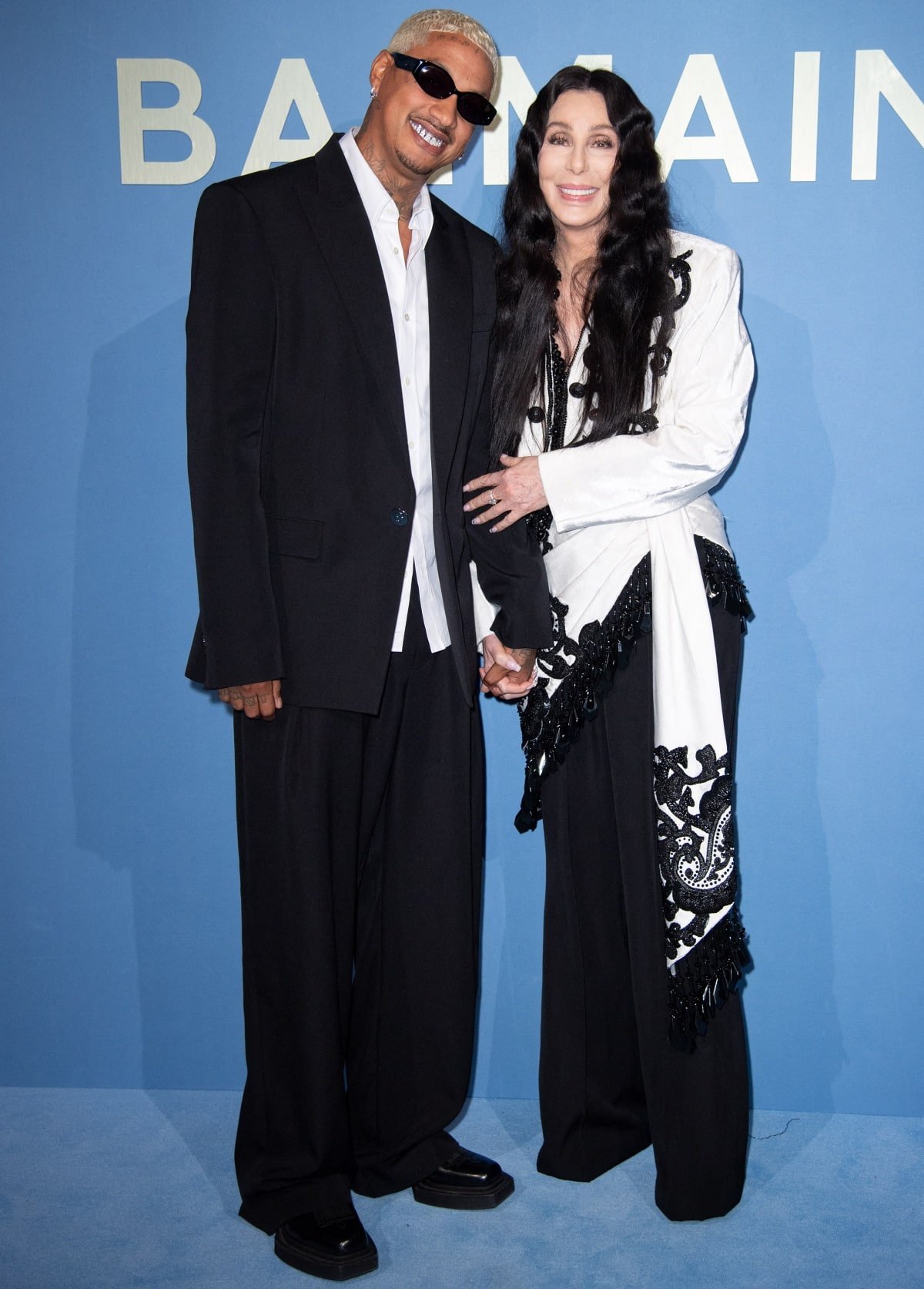 Alexander “AE” Edwards wearing an oversized black suit with a white button-down shirt, black square-toed platform shoes, and black sunglasses