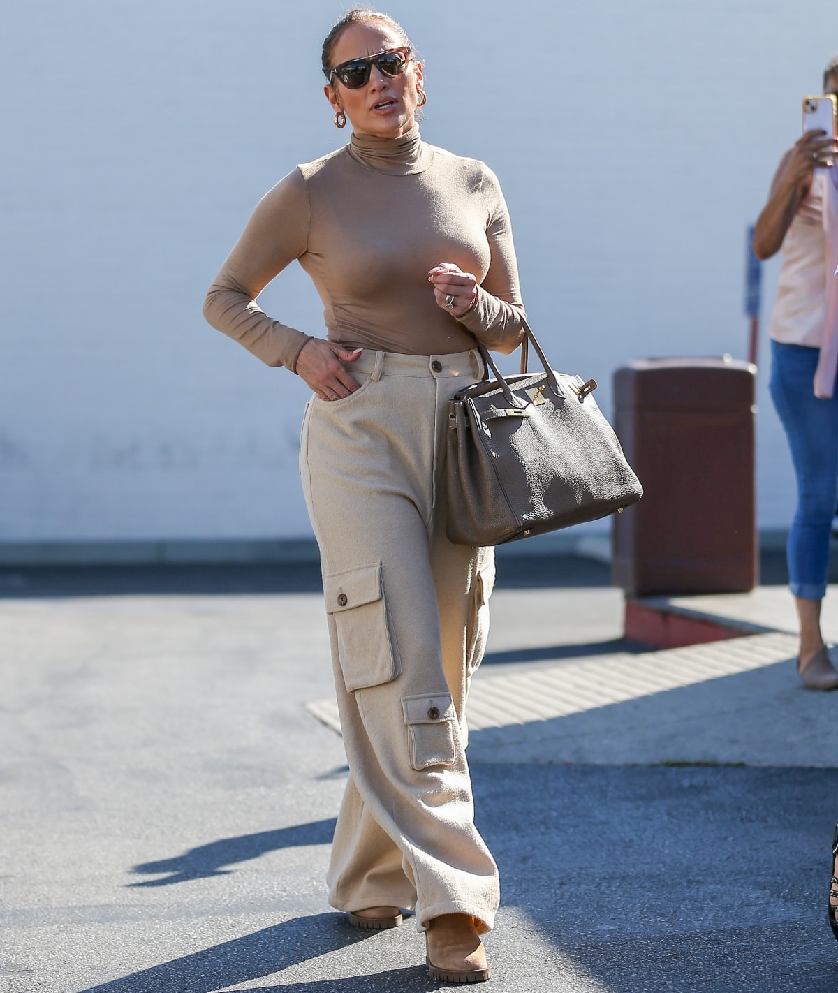 Jennifer Lopez carrying a pale brown Hermes Birkin 35 bag and accessorizing with gold hoop earrings, her Rahaminov diamond engagement ring, and tortoiseshell sunglasses