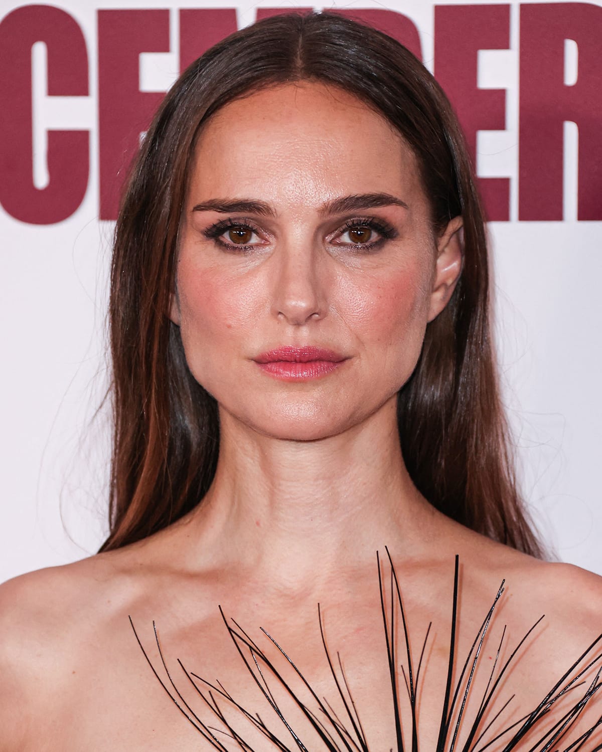 Natalie Portman styles her brunette hair straight and highlights her features with smokey eyeshadow, mascara, and pink lipstick