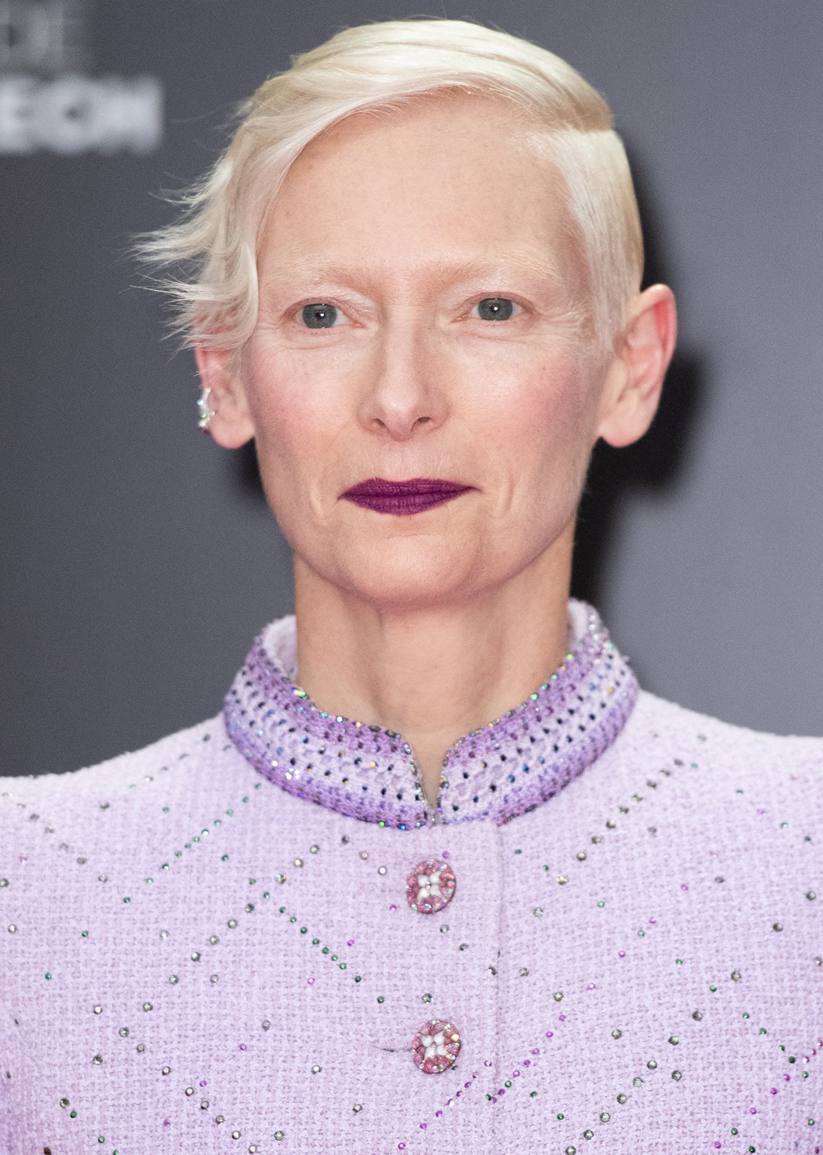 Tilda Swinton adds her signature edge to the look by wearing a single diamond earring and sporting deep purple lipstick