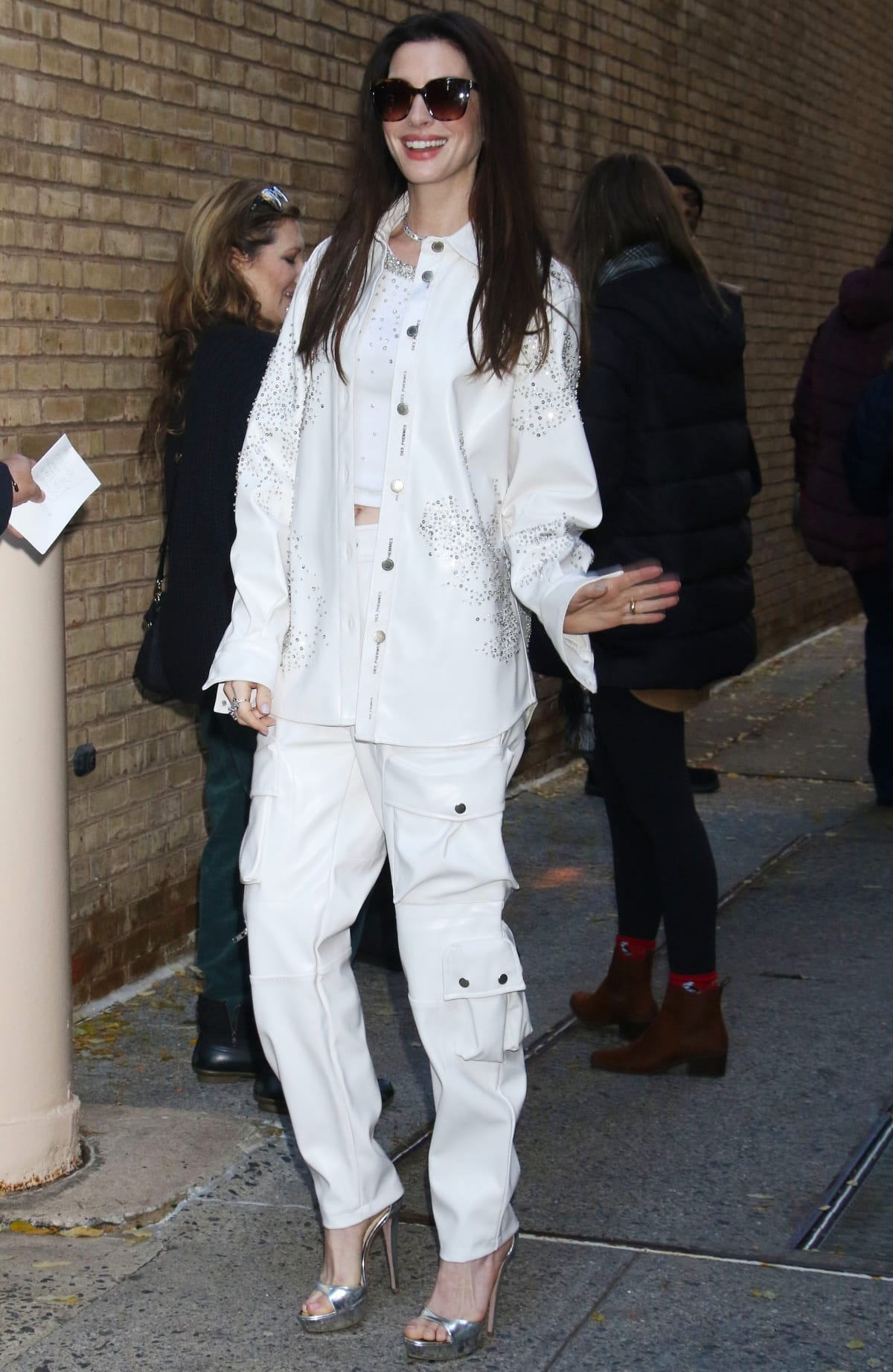 Anne Hathaway looking effortlessly chic in an all-white ensemble featuring an embellished crop top, cargo pants, and oversized jacket while outside the studios of Live with Kelly and Mark