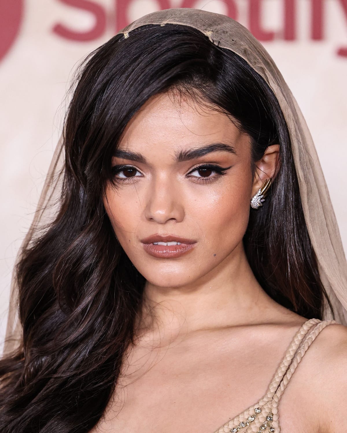 Rachel Zegler’s beauty look consisted of brunette waves, light bronze eye makeup, black winged liner, a nude-colored glossy lip, and Jean Schlumberger Flame silver earrings by Tiffany & Co.