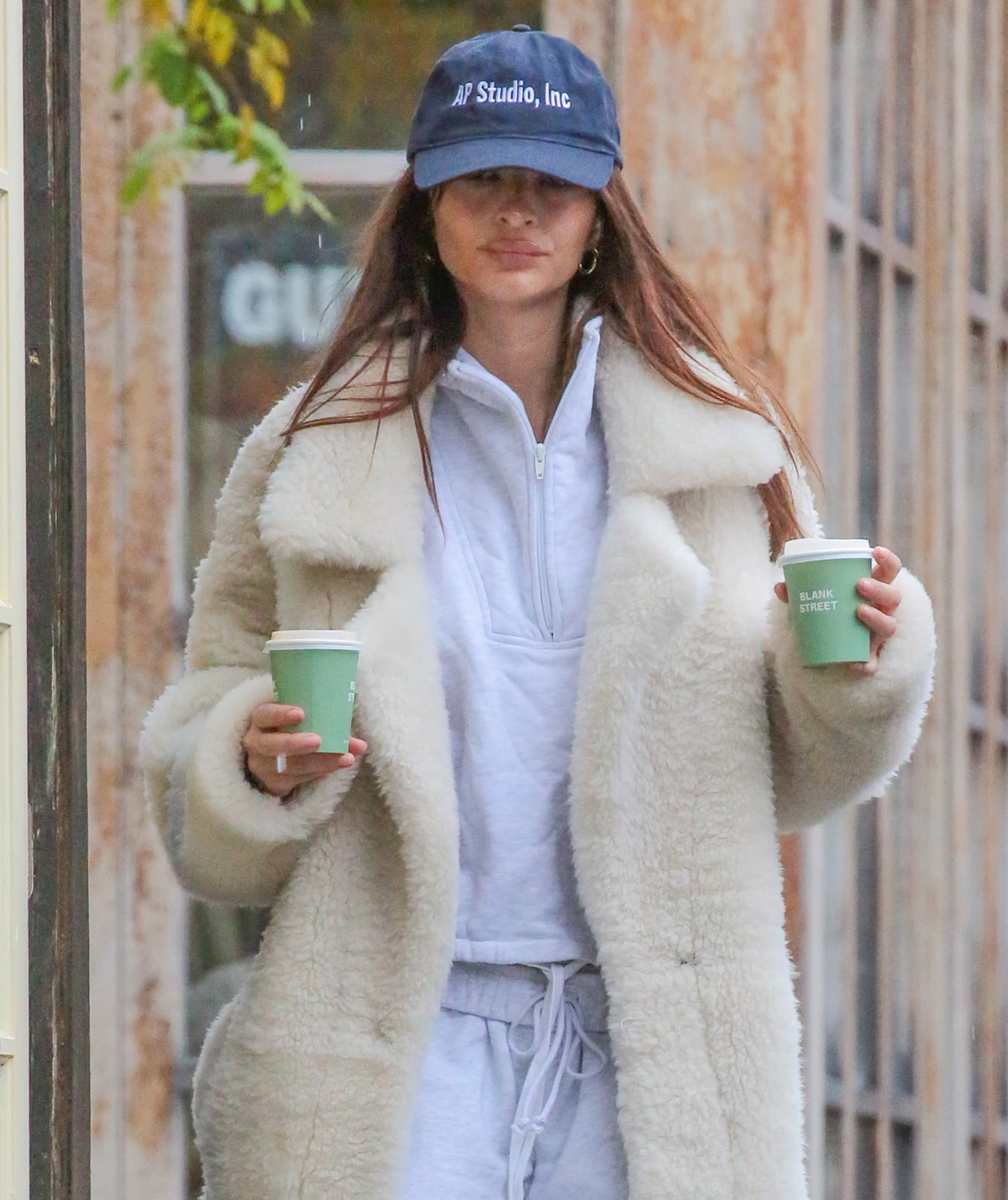 Emily Ratajkowski tucks her straightened brown hair beneath her AP Studio, Inc. baseball cap and wears her signature nude makeup for her casual stroll