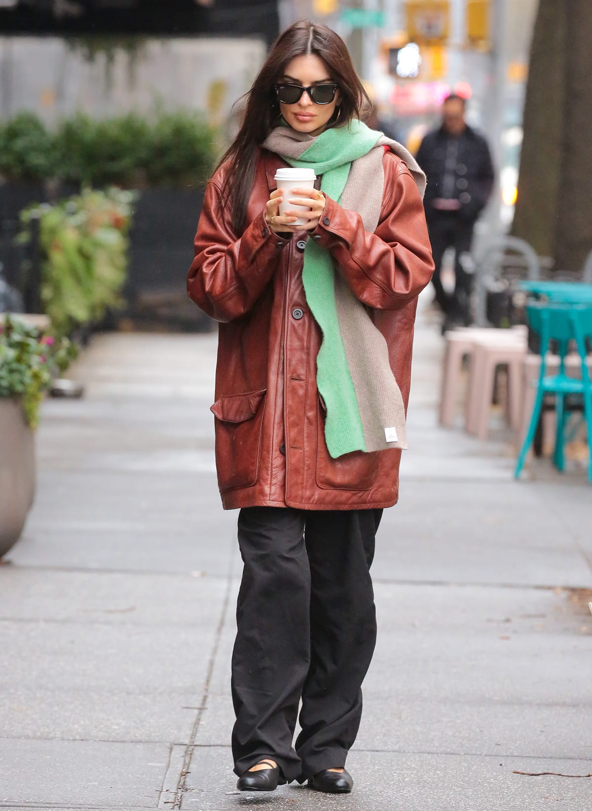 Emily Ratajkowski bundles up in a terracotta leather coat, a beige and green scarf, black pants, and ballet flats while on a coffee run in New York City on December 27, 2023