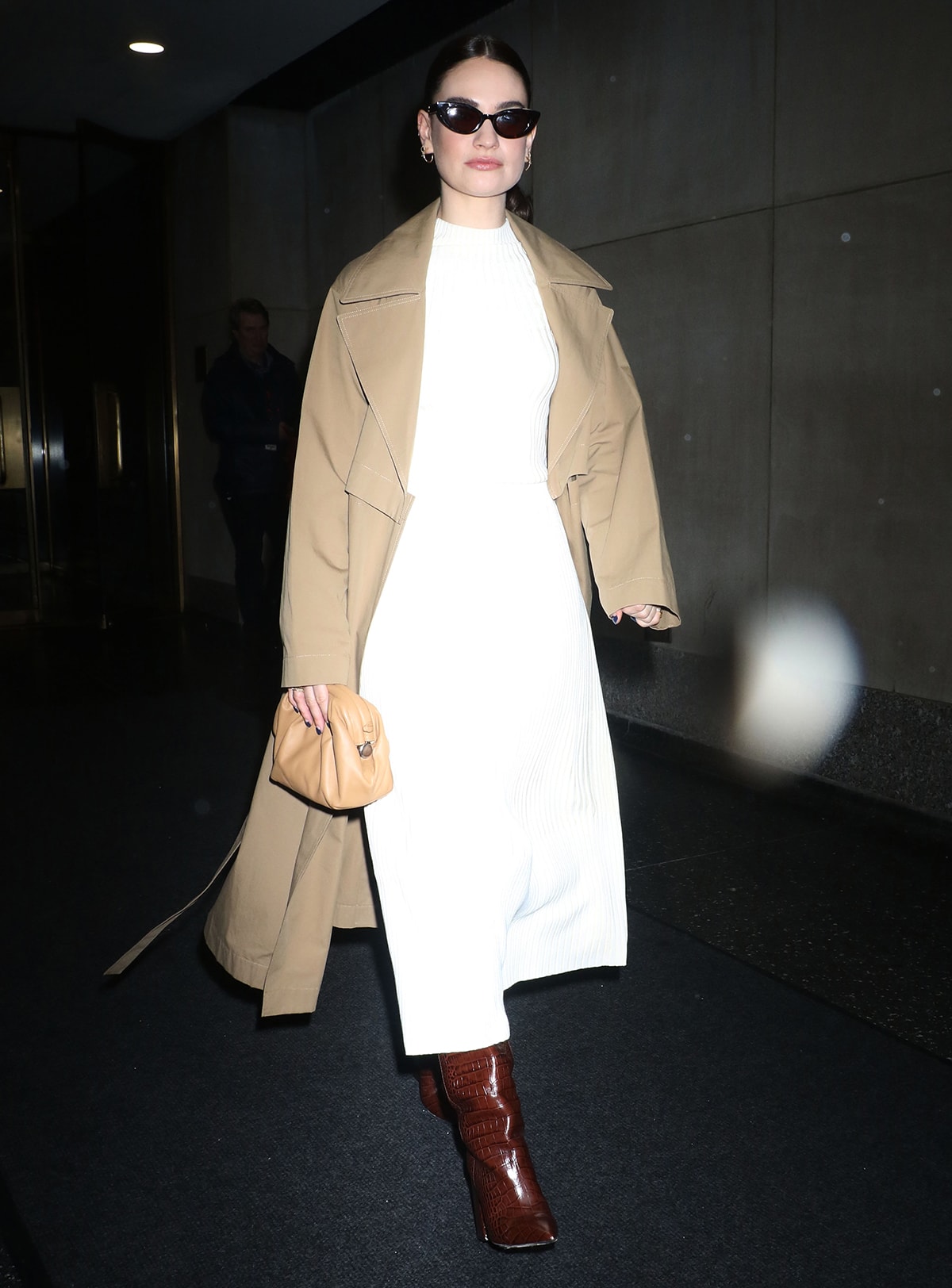 Lily James is warmly dressed as she pairs her rib-knit outfit with a khaki trench coat and a pair of Paris Texas croc-embossed knee-high boots