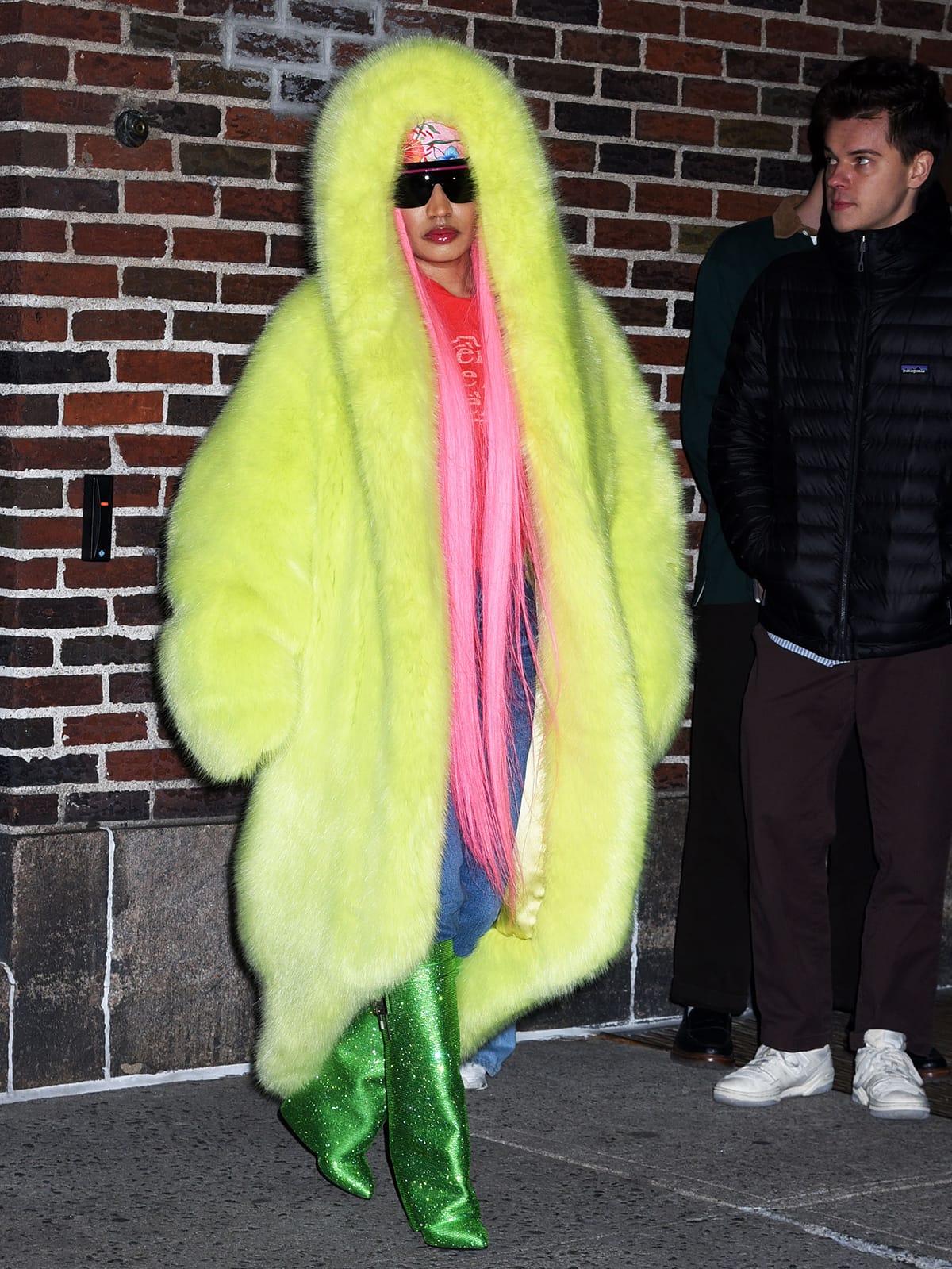 Nicki Minaj embraces maximalist styling with a thick yellow fur coat, a hot pink tee, blue jeans, and green boots as she leaves the Ed Sullivan Theater on December 11, 2023