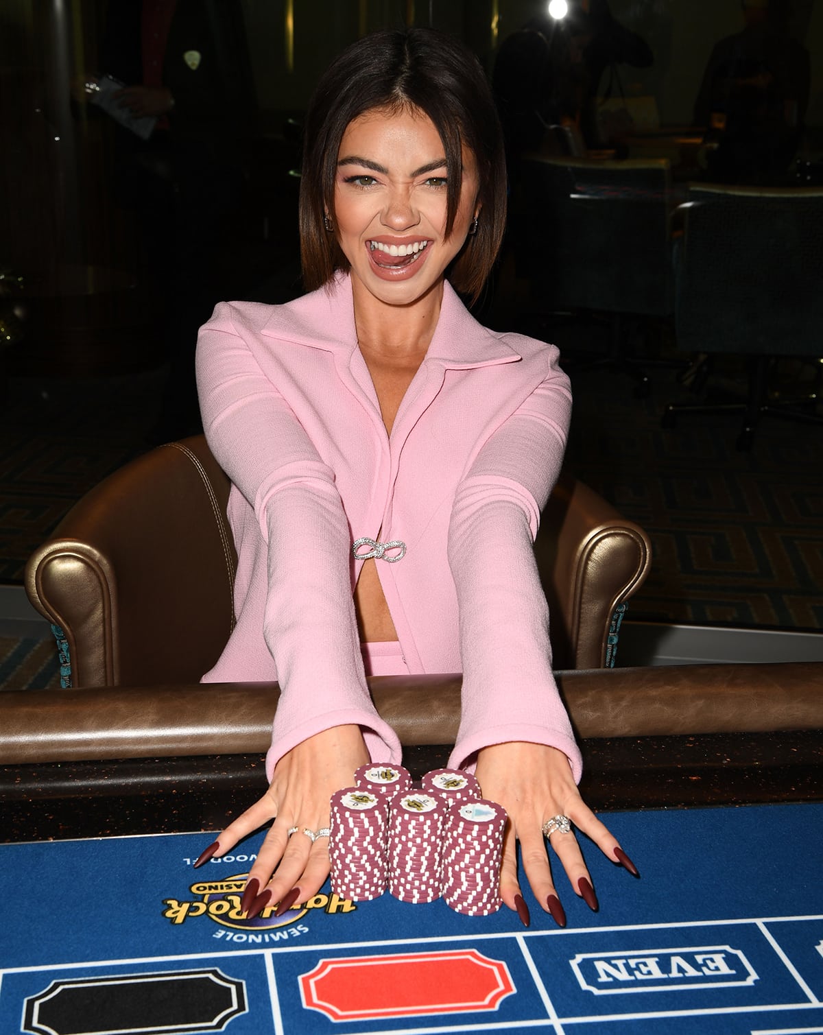 Sarah Hyland styles her Barbie pink outfit with Walters Faith earrings, diamond rings, and fake long nails and highlights her green eyes with mascara and neutral eyeshadow