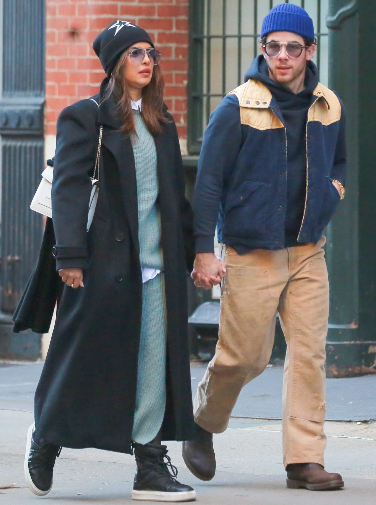 Nick Jonas wearing a black pullover with a navy jacket, beige pants, and a royal blue beanie