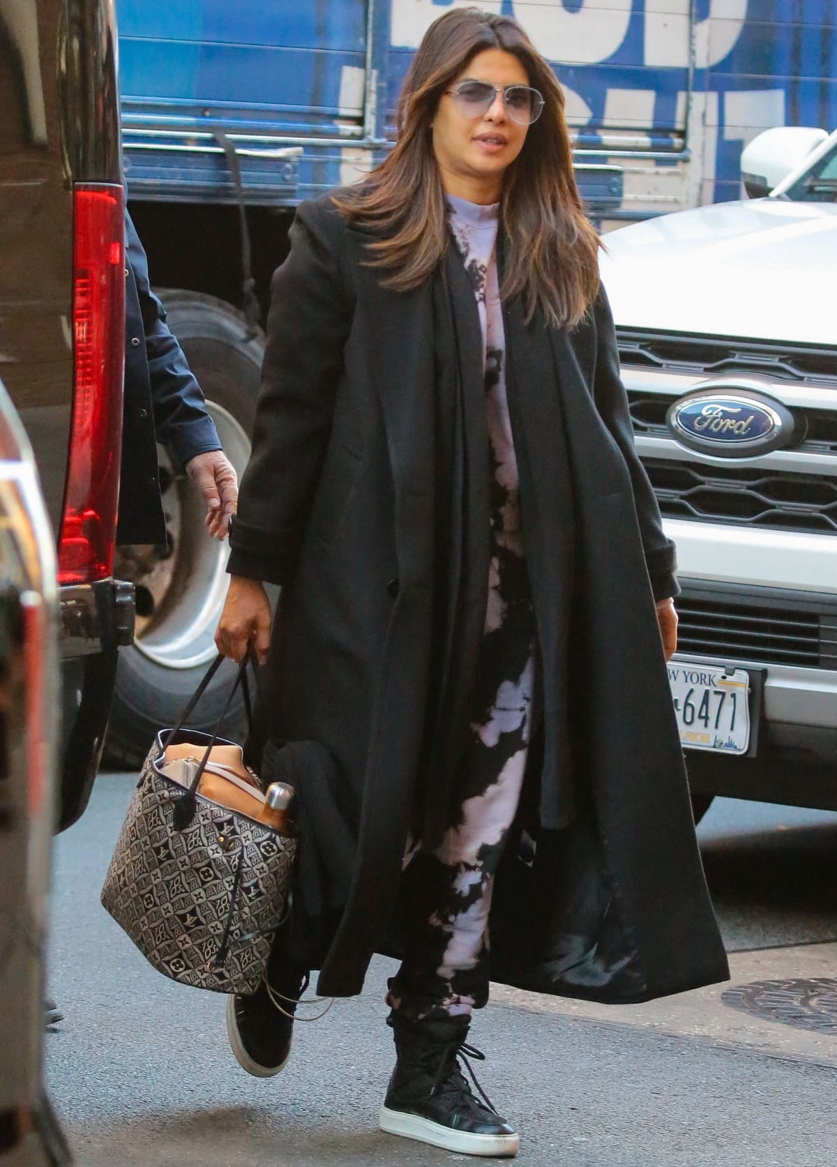 Priyanka Chopra wearing a purple-and-black spotted sweatsuit layered under an oversized black trench coat while out and about in New York City