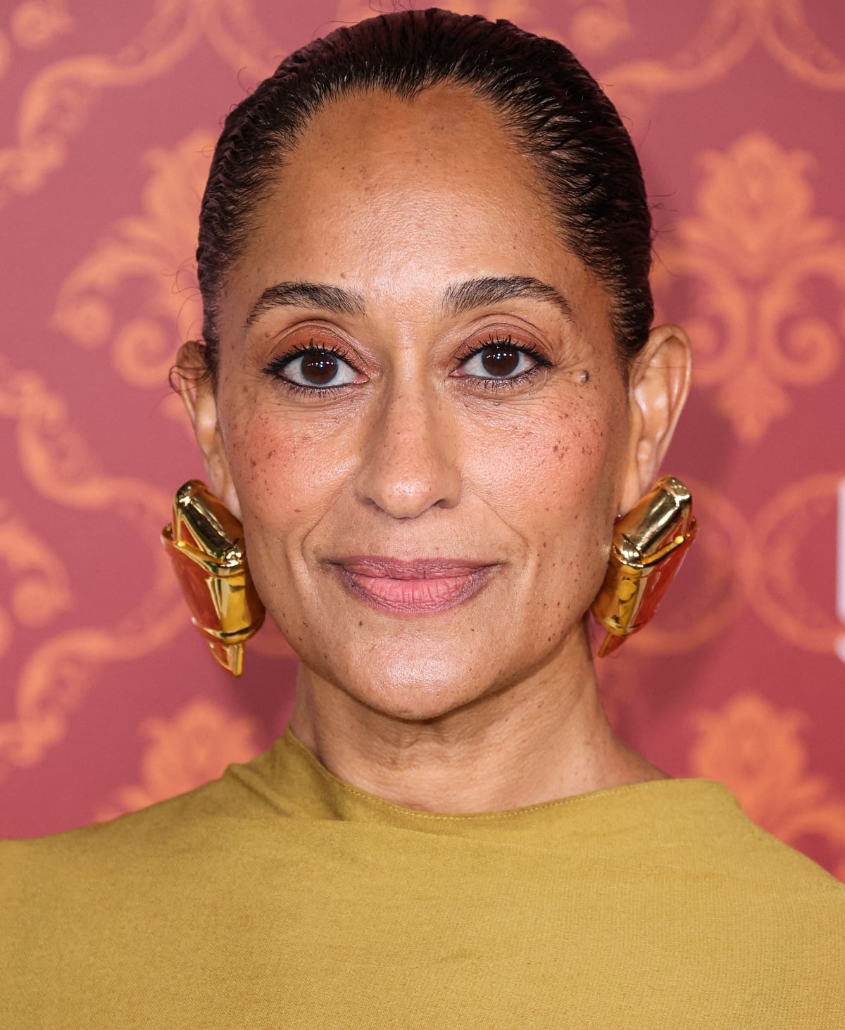 Tracee Ellis Ross’ beauty look consisted of warm eyeshadow, rosy cheeks, a pink lip, a sleek bun, and large abstract gold earrings