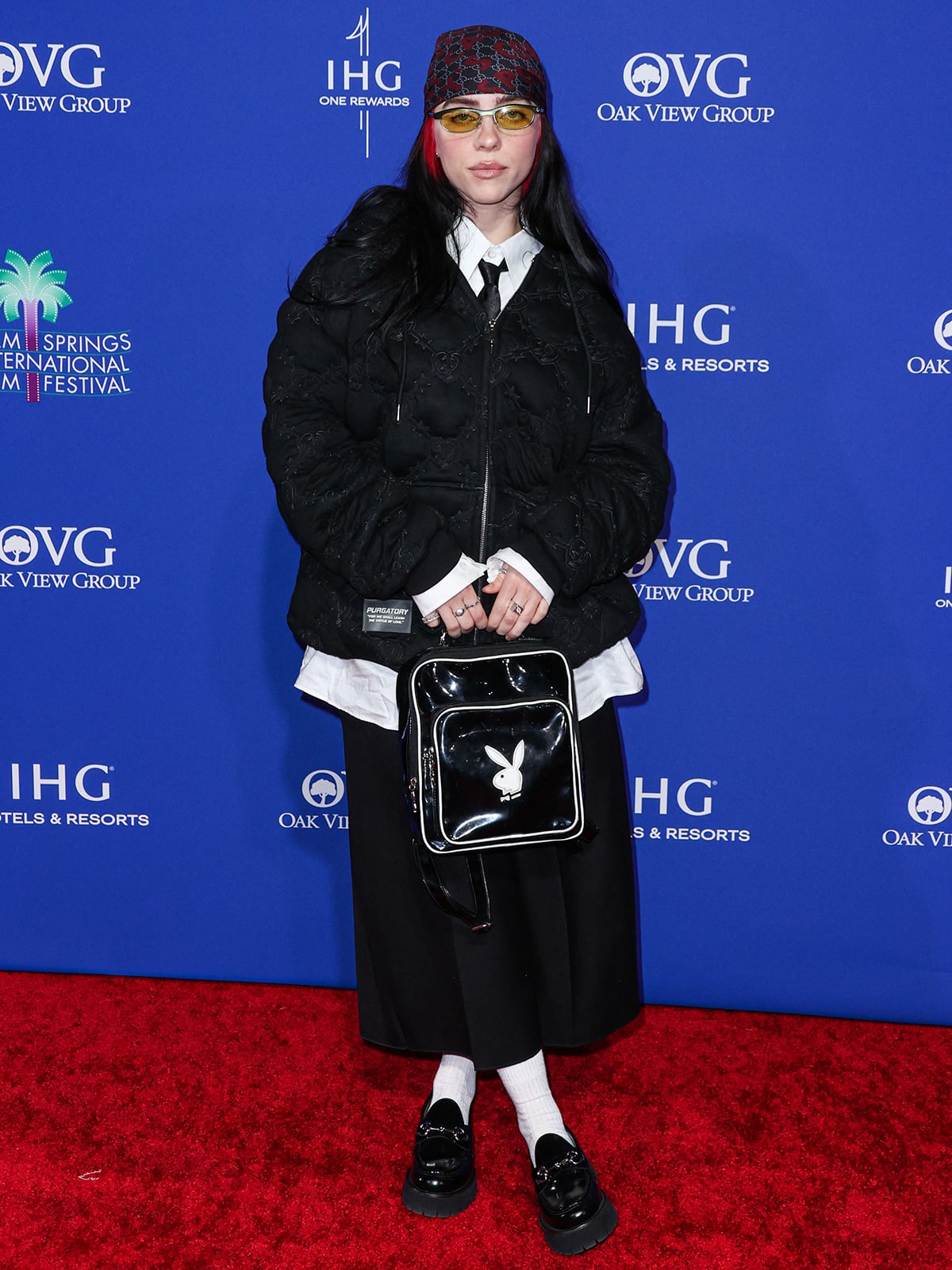 Billie Eilish dons an oversized black quilted puff hoodie by Purgatory, a white shirt and a slim black necktie underneath, a pair of black baggy crop pants, and black Gucci lug sole loafers