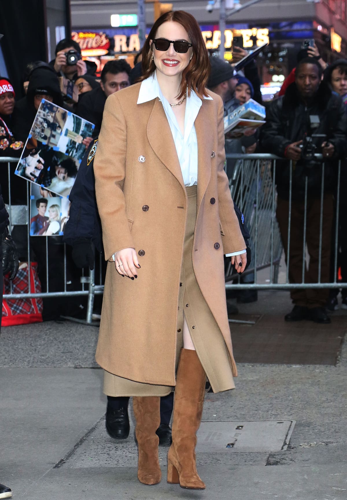Emma Stone makes a stylish entrance at the Good Morning America studios in a blue Louis Vuitton shirt, a caramel midi skirt, matching boots, and a camel coat on January 30, 2024