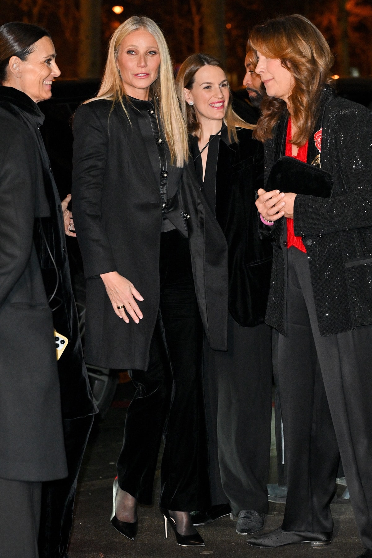 Gwyneth Paltrow's chic all-black ensemble, blending Armani's elegance with a hint of Matrix-style, includes a fitted top with pearl buttons and straight-leg trousers, complemented by a sleek black overcoat and pointed-toe stilettos