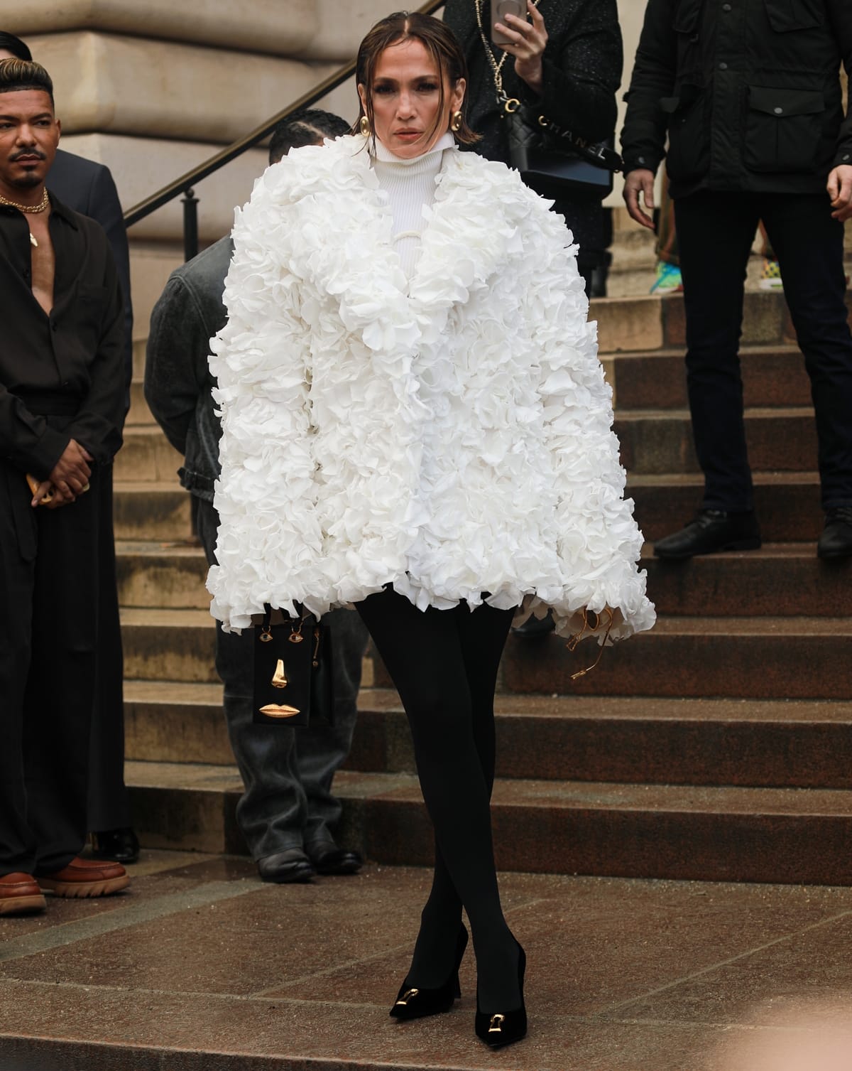 Jennifer Lopez captivated at Schiaparelli's Haute Couture Fashion Week in Paris, donning a bespoke coat by Daniel Roseberry, intricately crafted from real white rose petals, enhanced with a silver moon face and sequined rays, complemented by a ribbed turtleneck