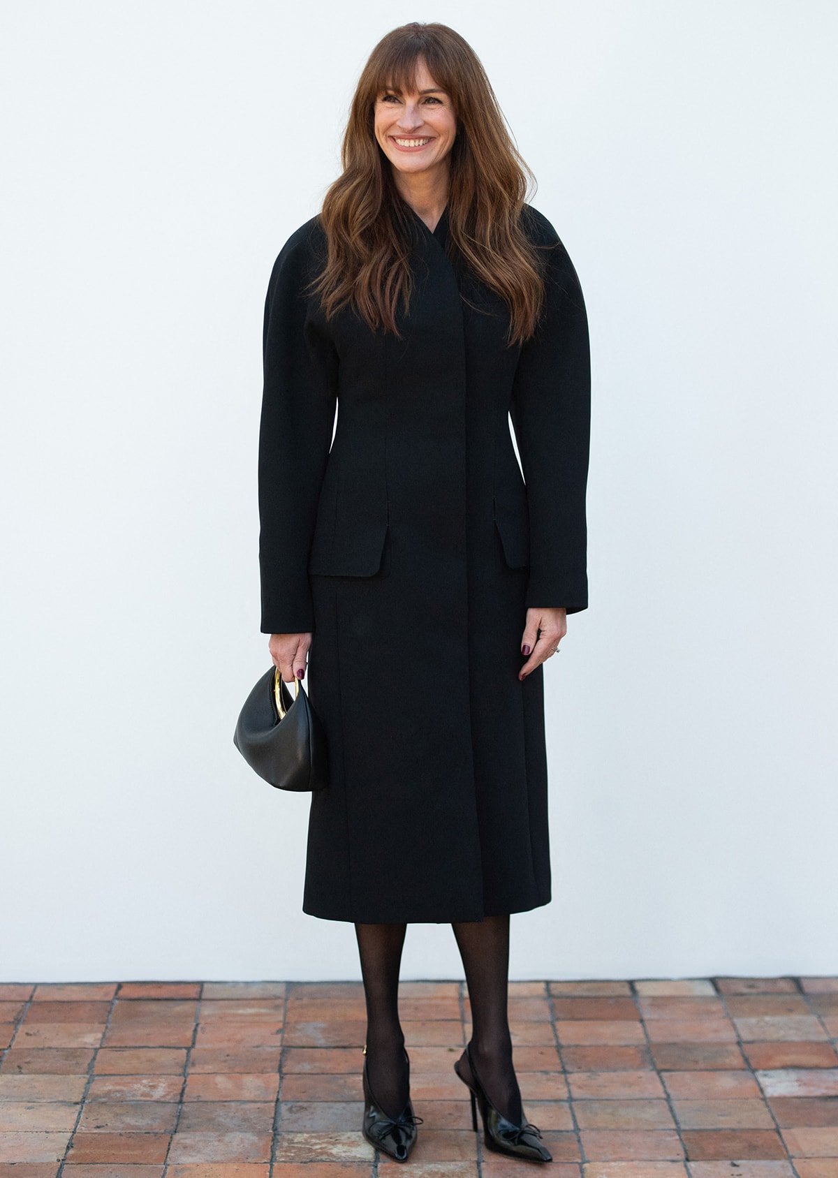 Opting for a regal look, Julia Roberts embraces quiet luxury in a structured black Jacquemus coat dress, sheer tights, and Jacquemus Les Slingbacks Cubito Hautes shoes