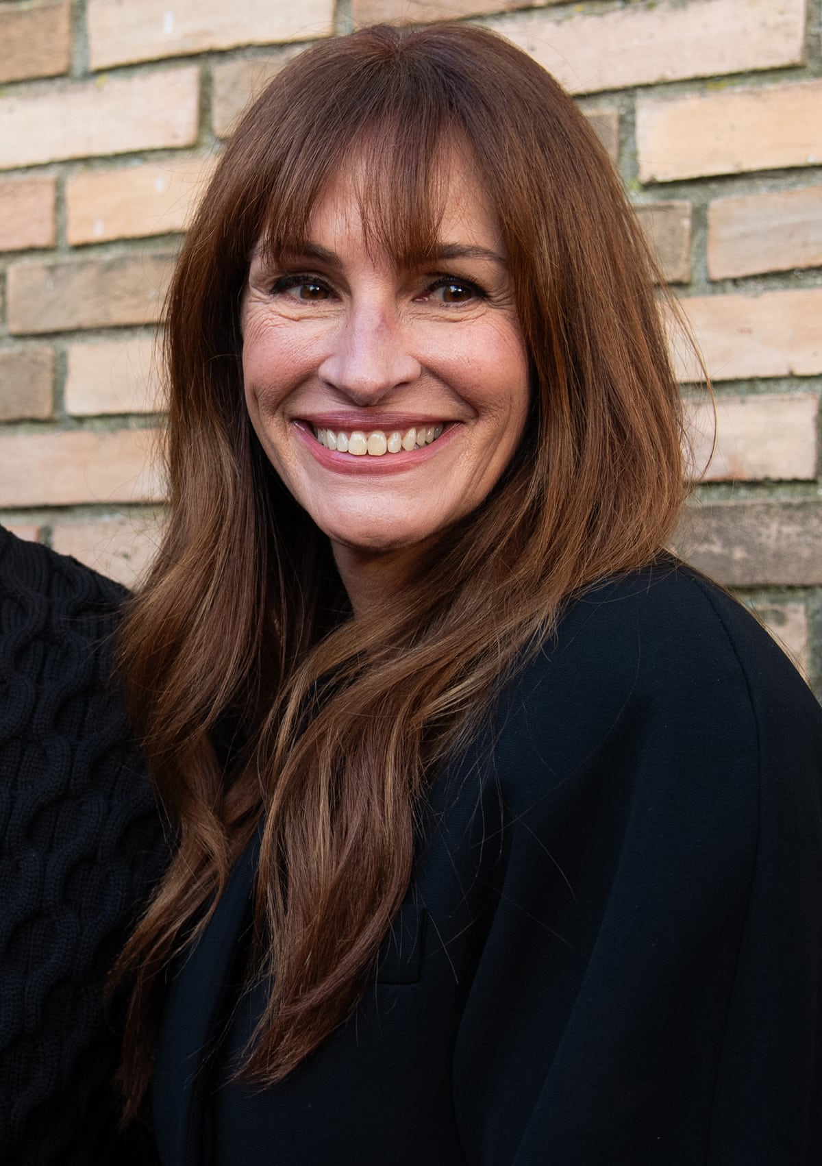 Julia Roberts enhances her natural beauty with soft pink makeup and wears her chocolate tresses in waves with face-framing bangs