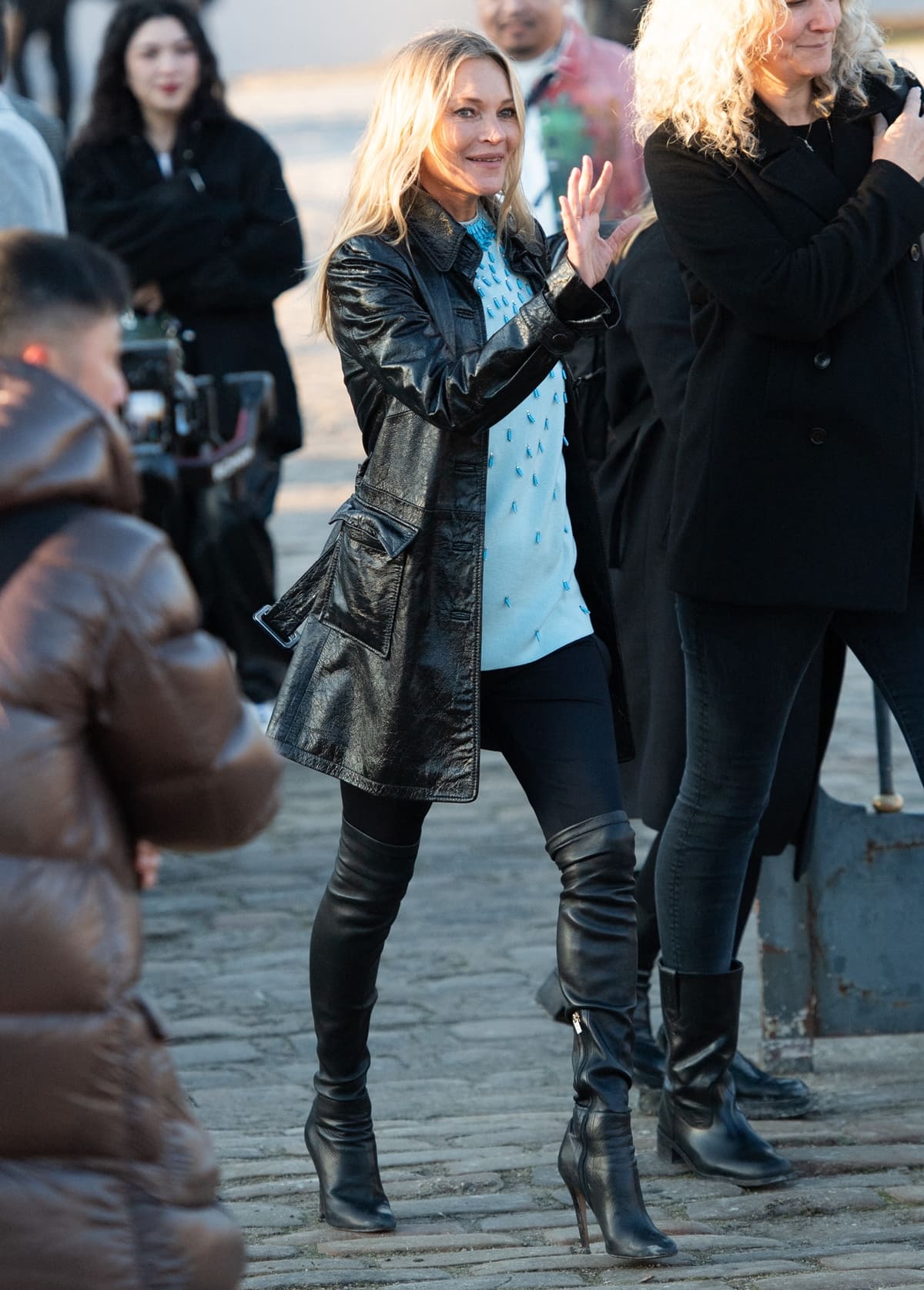 Kate Moss exudes contemporary glamour in a sleeveless aqua top, intricately adorned with cascading turquoise bead embellishments and tiered stone collars, paired with sleek black leggings and statement over-the-knee leather stiletto boots