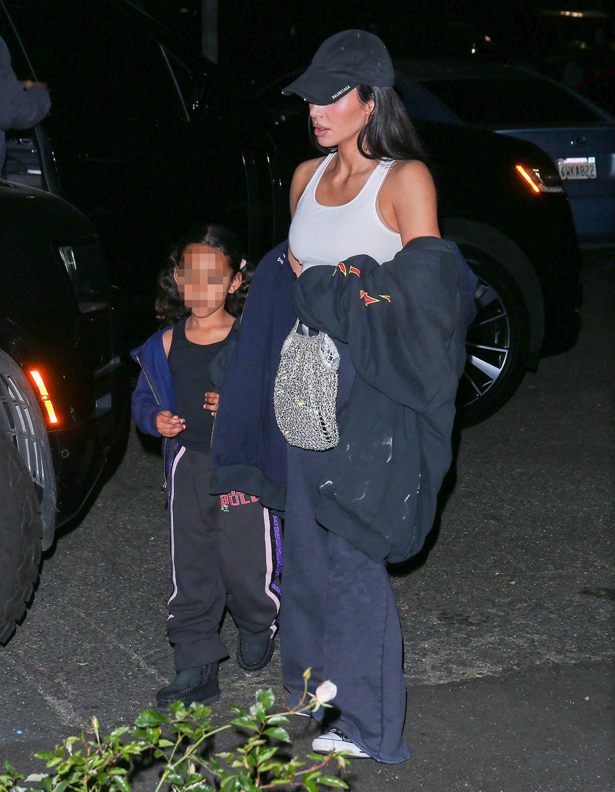 Kim Kardashian flaunts her toned arms and abs in a white rib-knit crop top, flared sweatpants, and sneakers while Chicago dons a sporty tank top, jogging pants, and black shoes