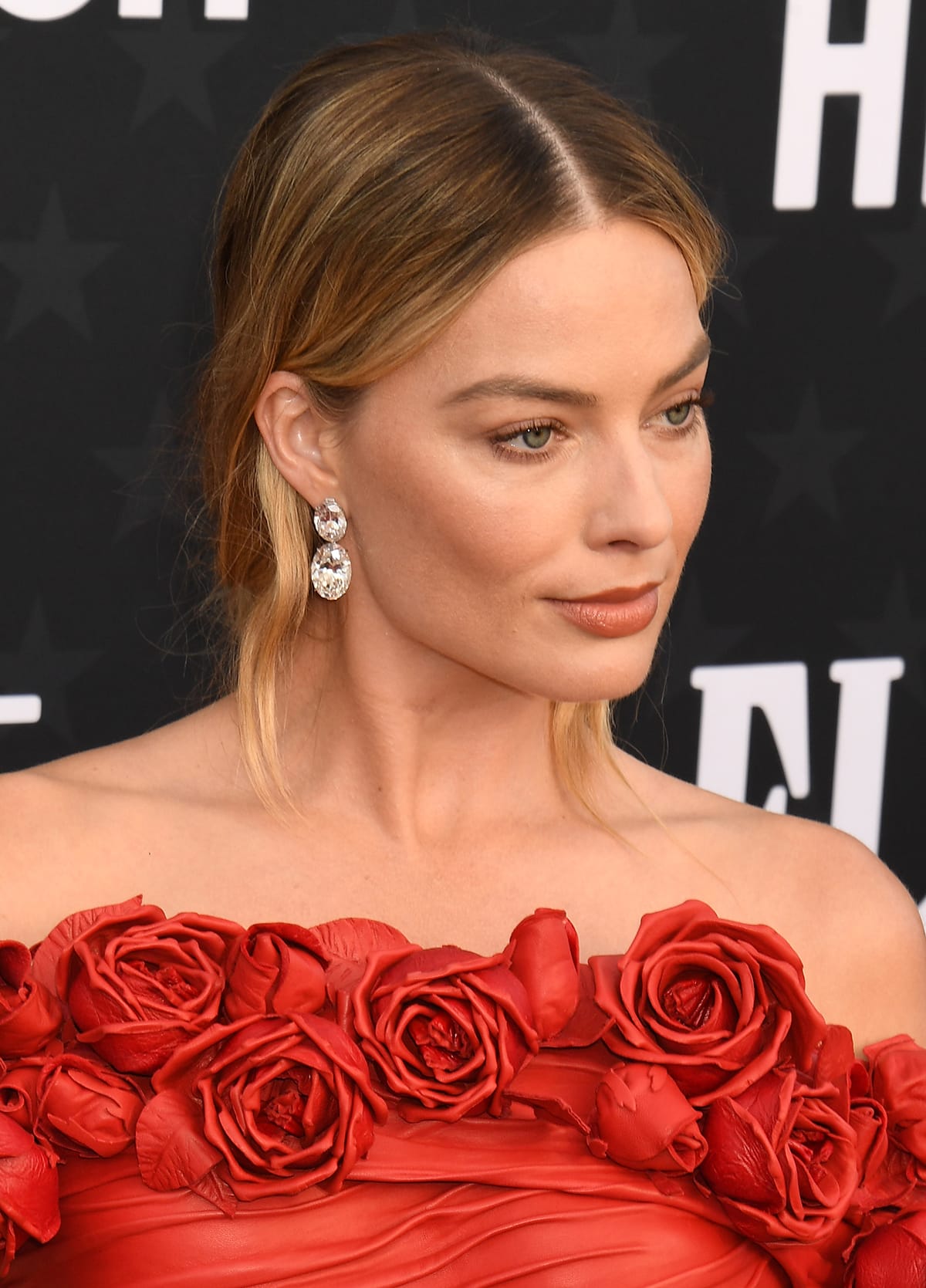 Margot Robbie wears her tresses in a loose low bun and highlights her natural beauty with minimal makeup that includes mascara, subtle blush, and red-brown lipstick