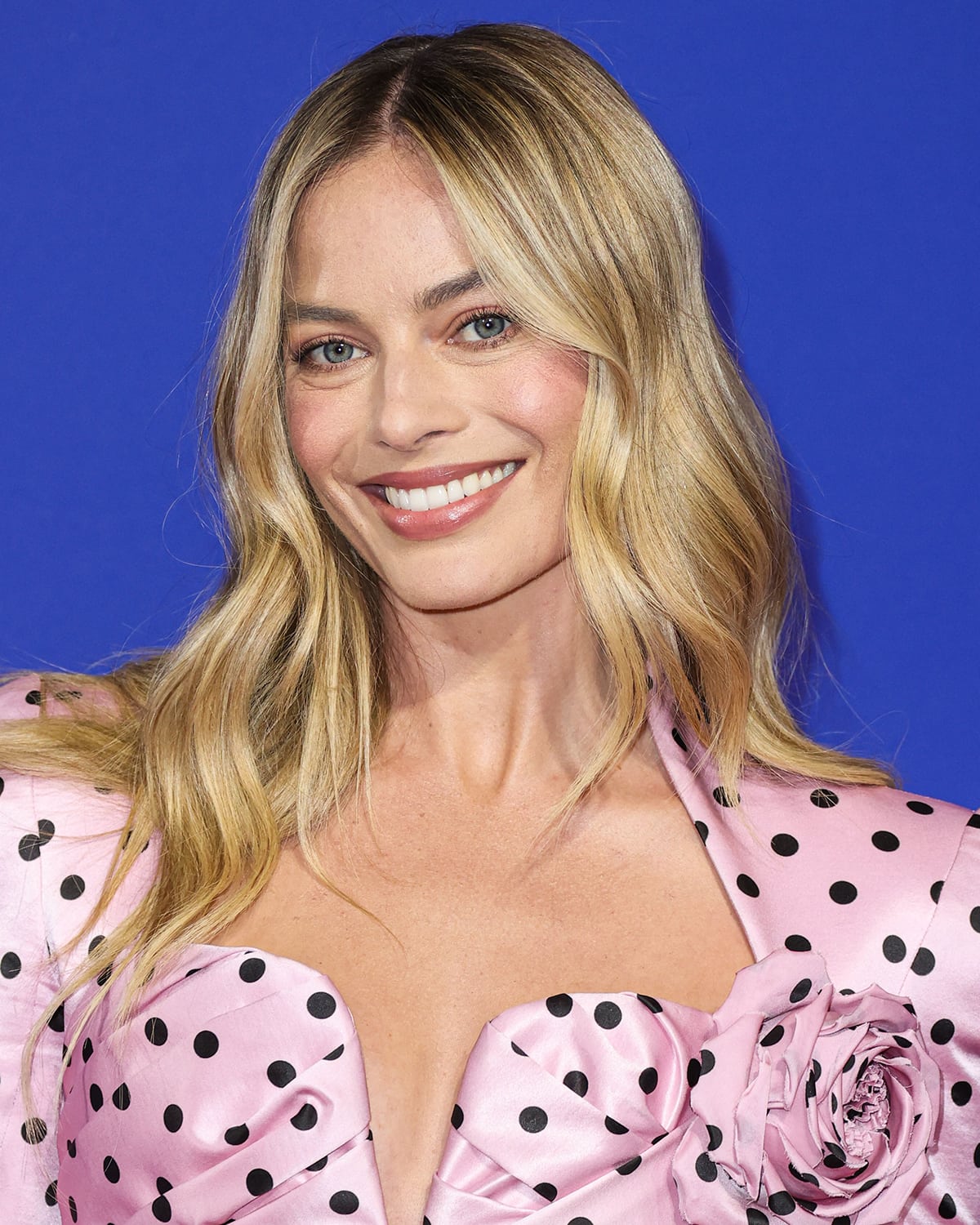 Margot Robbie styles her blonde hair in loose waves and wears Barbie-esque light pink makeup with mascara to highlight her blue eyes