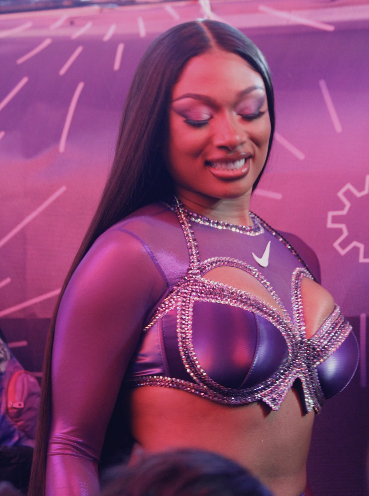 Megan Thee Stallion stuns in an all-purple-themed look with a custom Nike cutout crystal-embellished bralette, matching tight-fitting pants, and purple eyeshadow