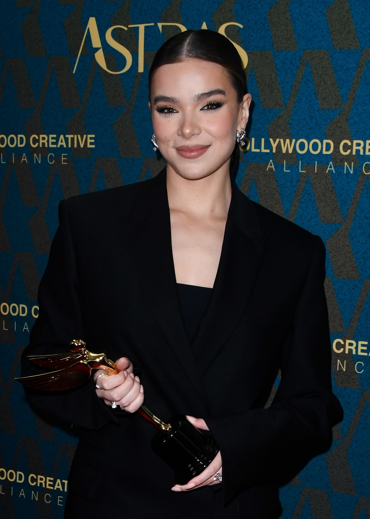 Hailee Steinfeld's makeup featured a nude lip, complemented by a middle-parted low updo adorned with a black silk bow, capturing a look of refined sophistication