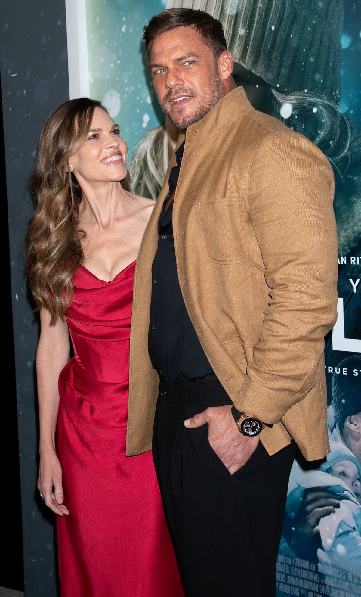 Alan Ritchson, towering at 6ft 2in (188 cm), exudes charm beside a comparatively petite Hilary Swank, who stands at 5ft 6in (167.6 cm), both making a striking pair at the 'Ordinary Angels' premiere in New York City, with Ritchson in a stylish camel blazer and black shirt at the SVA Theater