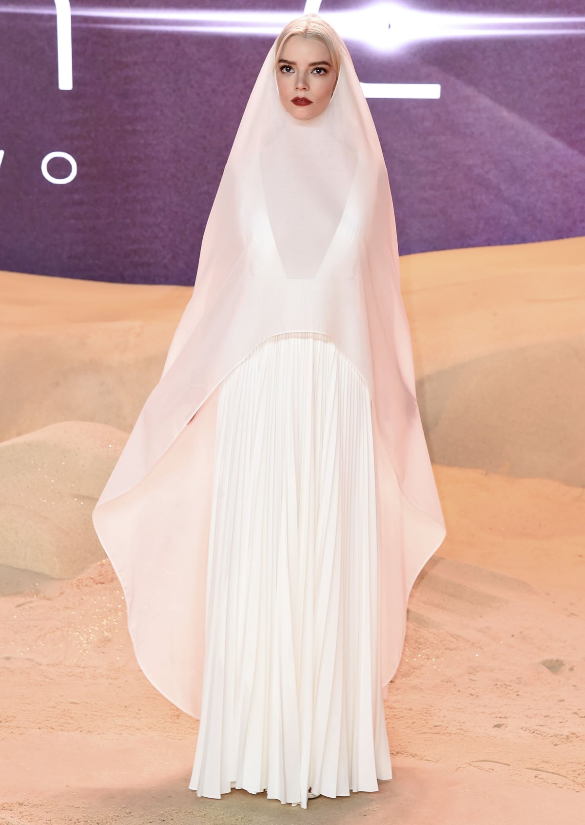 Anya Taylor-Joy strikes a pose in a vintage-inspired Christian Dior Haute Couture gown featuring a daring square neckline and a translucent white hooded cape framing her face