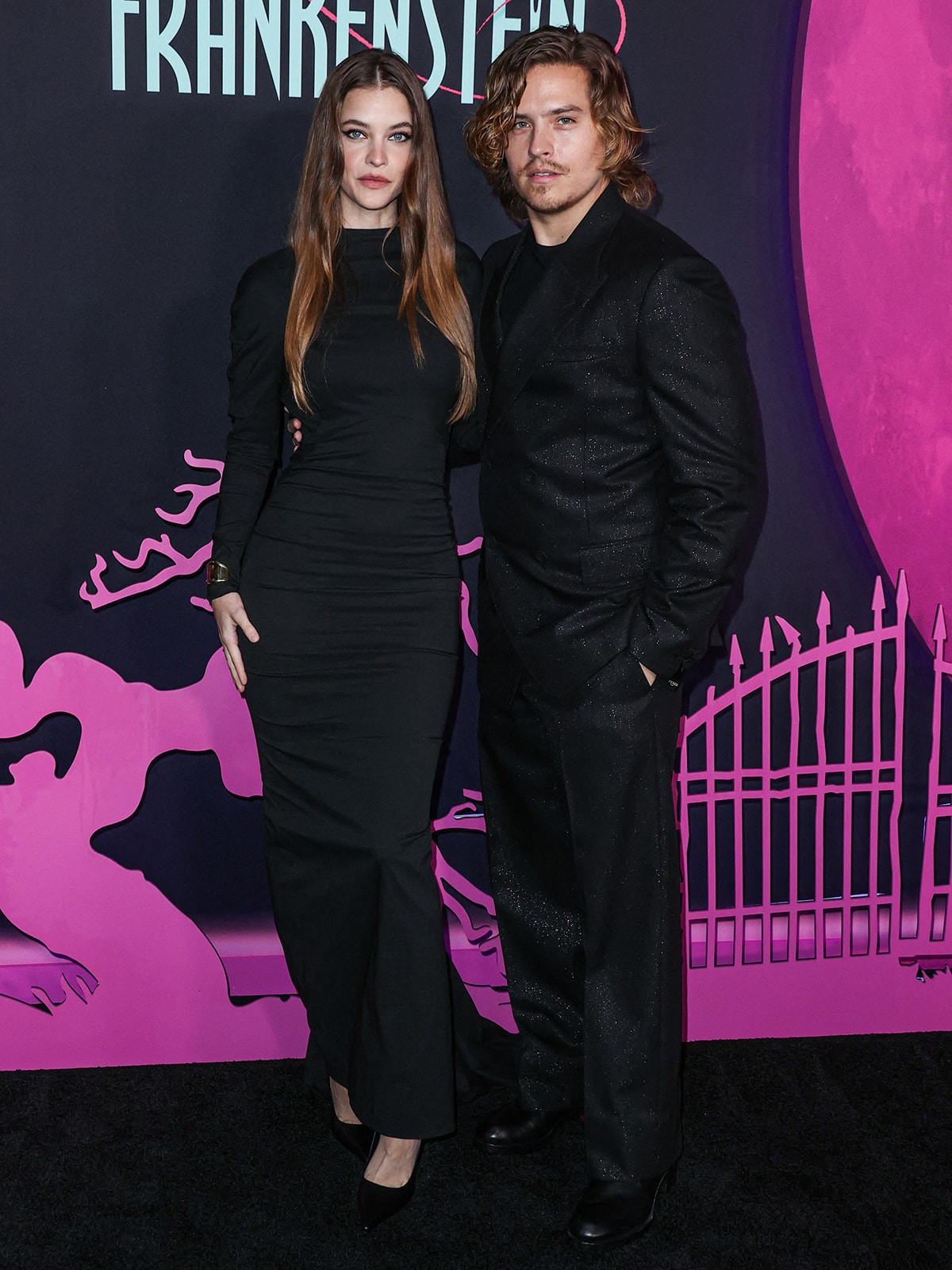 Barbara Palvin and Dylan Sprouse wear matching black ensembles, with Barbara in a Maison Alaia dress and Dylan in a shimmering black suit, at the Los Angeles premiere of Lisa Frankenstein to support Cole Sprouse