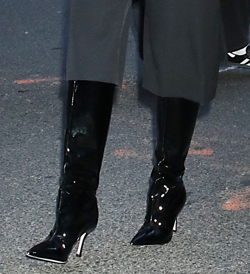 Camila Mendes teams her Bermuda shorts with black patent knee-high boots with sharp pointed toes and thin heels