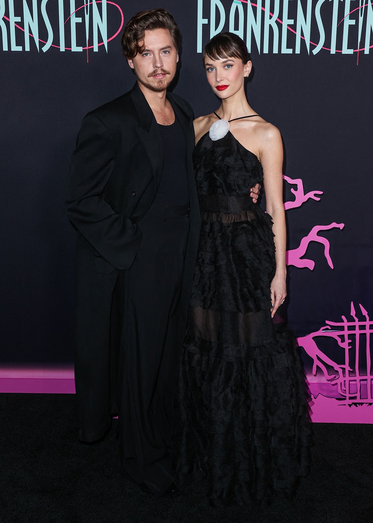 Cole Sprouse, wearing a black Balenciaga ensemble, wraps his arm around his girlfriend's tiny waist as they pose on the red carpet at the Hollywood Athletic Club in Los Angeles for the premiere of Lisa Frankenstein on February 5, 2024