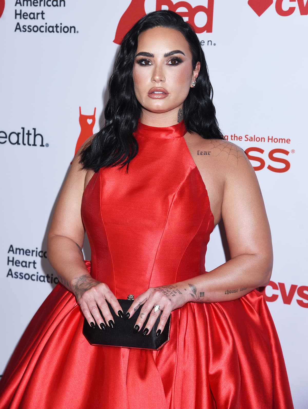 Demi Lovato shows off her arm tattoos and pear-shaped diamond engagement ring while holding a black Tyler Perry clutch