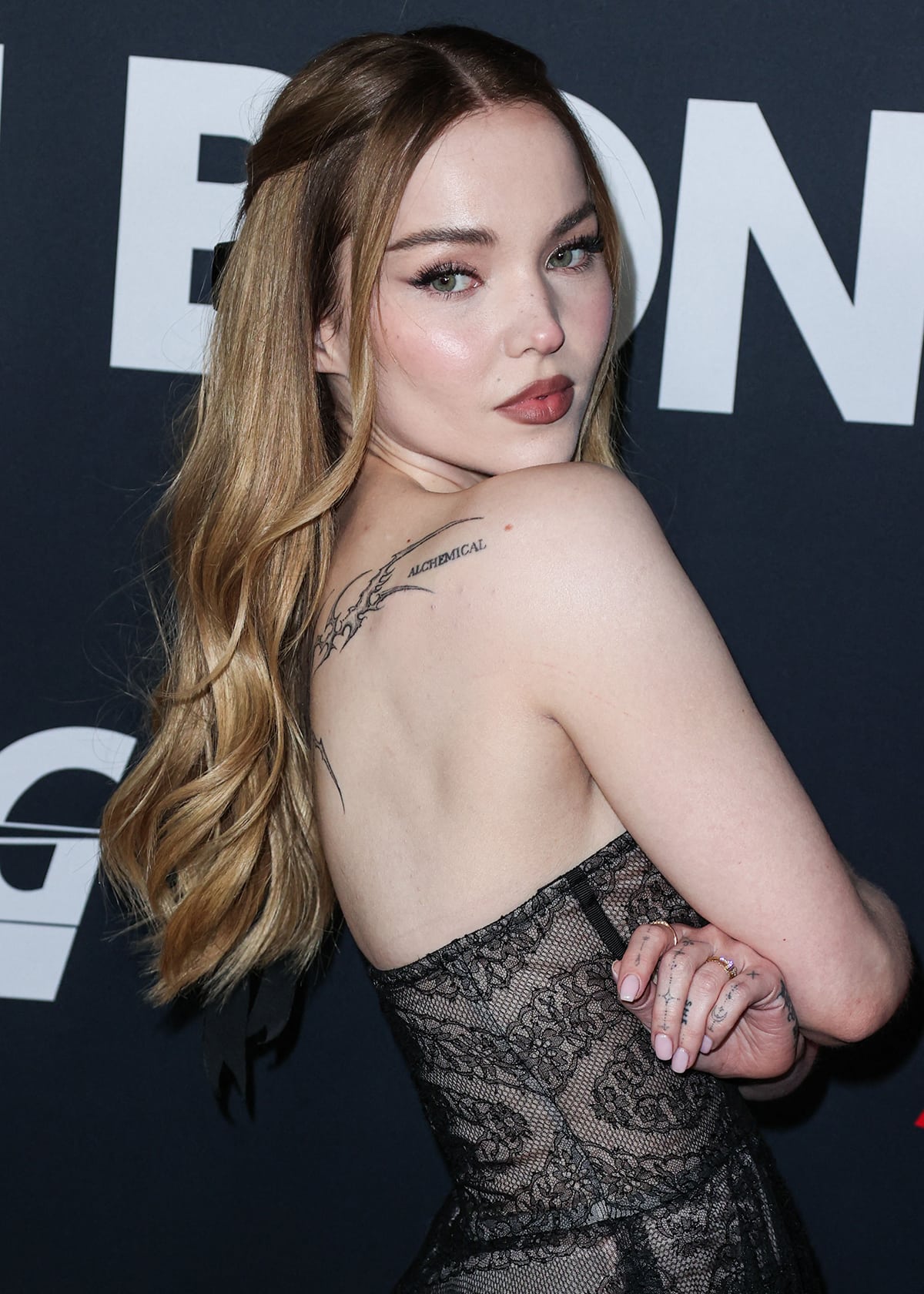 Dove Cameron glams up with fluttery lashes and pink makeup and styles her long blonde hair in a half-up ponytail