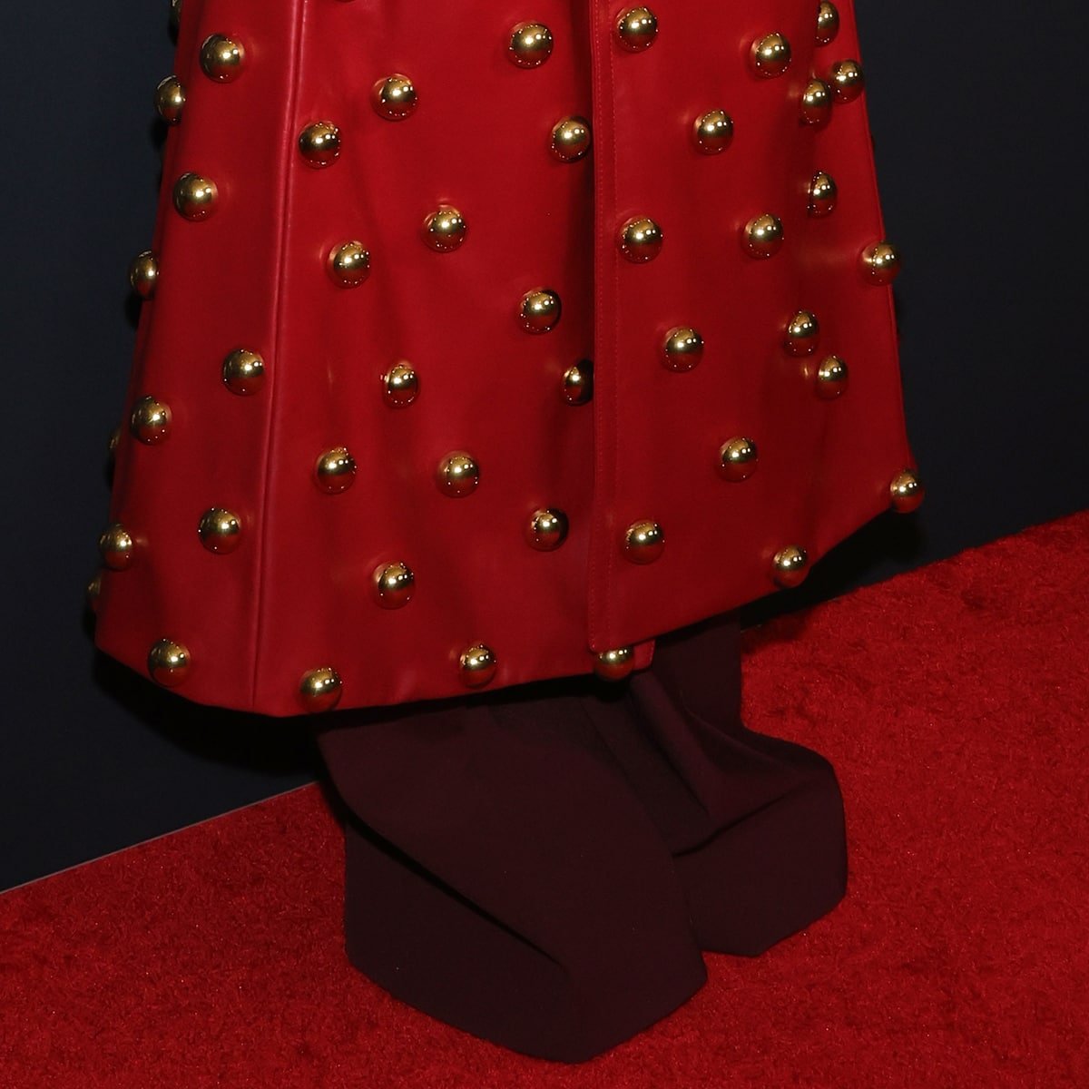 Dua Lipa's coat, adorned with gold ball studs and featuring an elongated silhouette, was paired with deep maroon trousers, concealing her footwear