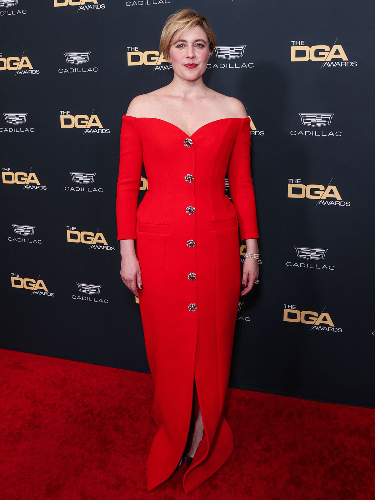 Honored with the DGA Film Feature medallion, Greta looks stunning in her red gown with silver pointed-toe pumps and a three-strand pearl bracelet