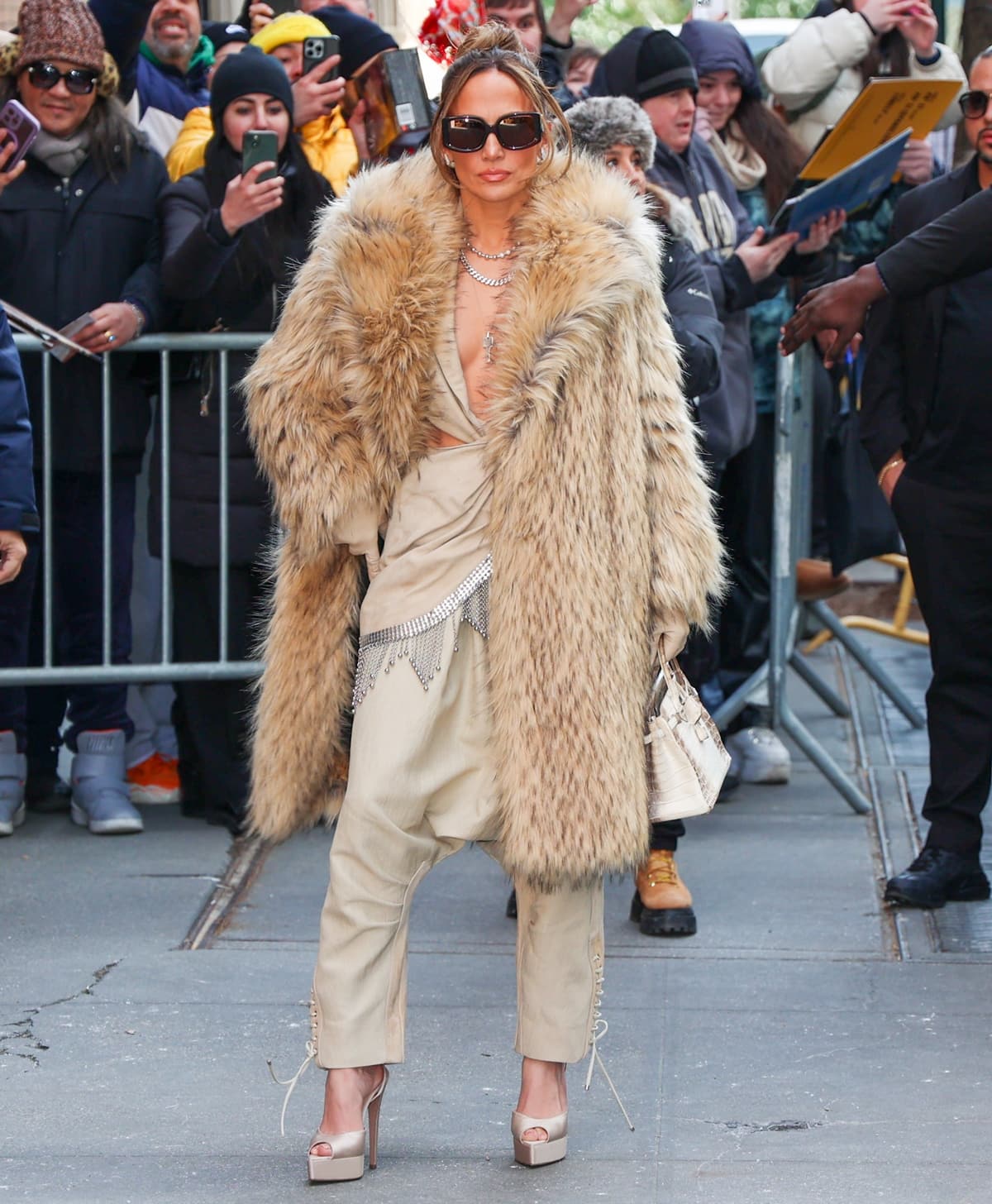 Jennifer Lopez wraps up her press day in a luxurious brown faux fur coat over a glamorous beige jumpsuit, showcasing her timeless style and flair for dramatic outerwear on February 15, 2024