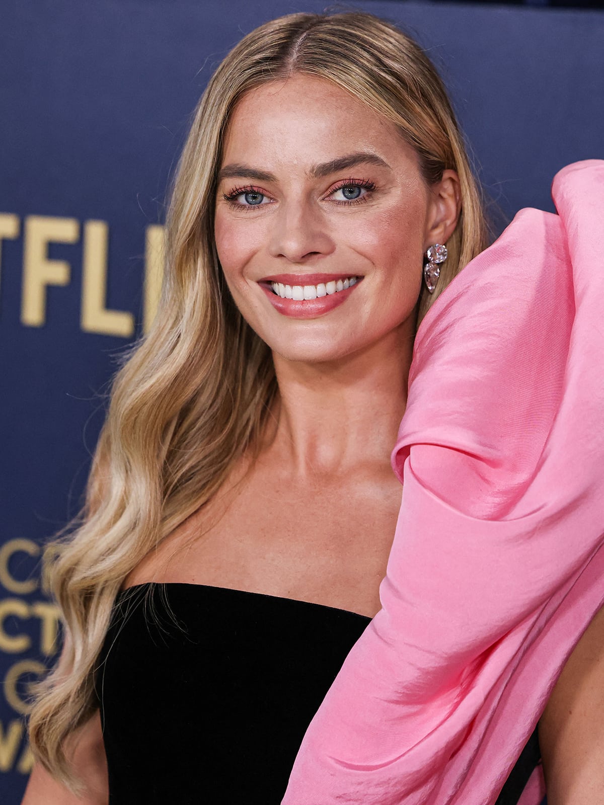 Margot Robbie opts for a wavy hairstyle and a Barbie makeup look, wearing soft pink eyeshadow, blush, and lipstick