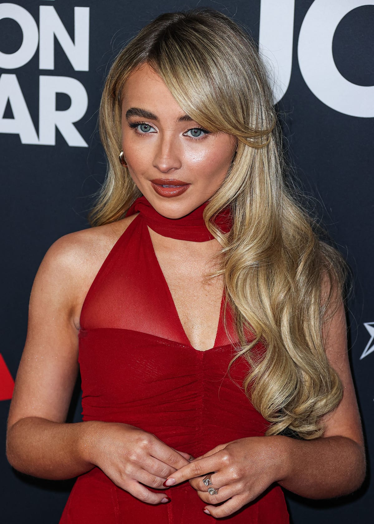 Sabrina Carpenter parts her wavy blonde hair to the side and highlights her striking features with rosy makeup