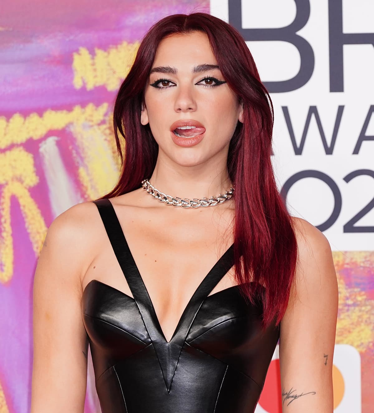 Dua Lipa wears Cleopatra-inspired eyeliner with nude lips and styles her burgundy hair down cascading over her shoulder