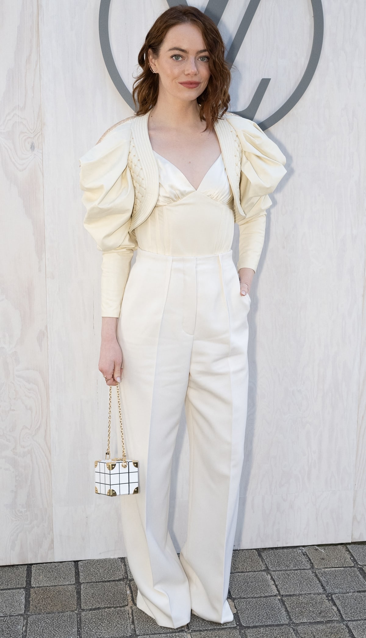 Emma Stone channels her character Bella Baxter at the Louis Vuitton PFW show in a cream corset top, mini quilted puff-sleeve jacket, and white high-waisted slacks